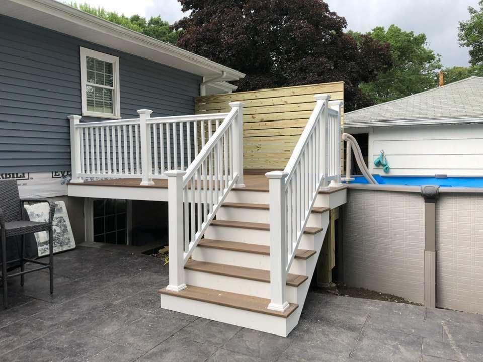 A deck with stairs leading to an above-ground pool. White railings, tan steps, and blue house siding.