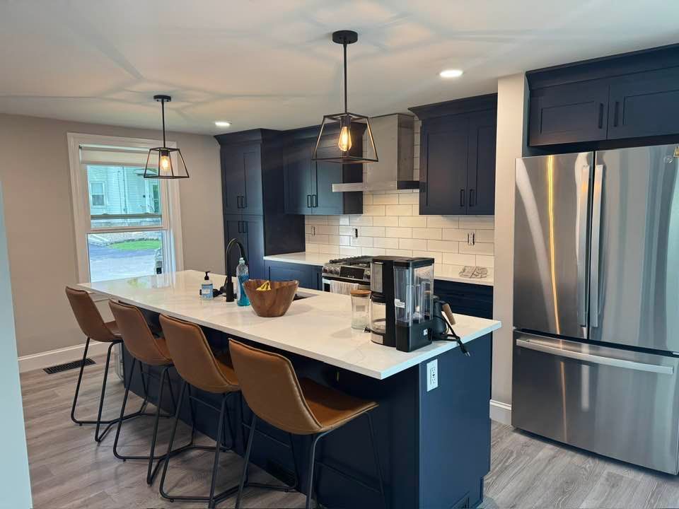 Modern kitchen with navy cabinets, white countertop, and stainless steel appliances. Island with bar stools.