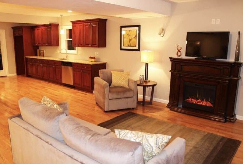 Living room with hardwood floors, built-in kitchen cabinets, fireplace, sofa, and armchair.