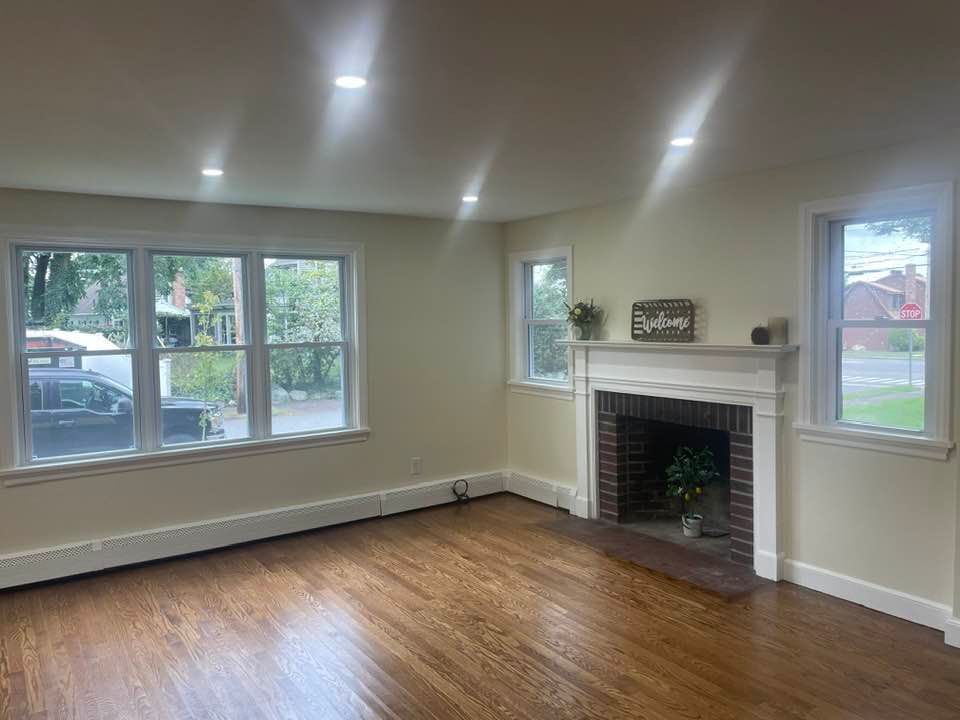 Living room with hardwood floors, windows, fireplace, and beige walls.