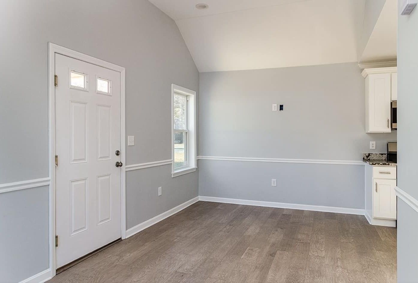 A mostly empty room with a white door, gray walls, and wood flooring.