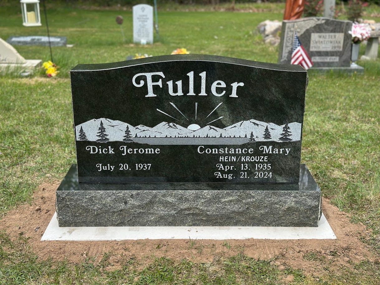 A black granite tombstone for the Fuller family with a mountain and sunrise engraving, set in a grassy cemetery.