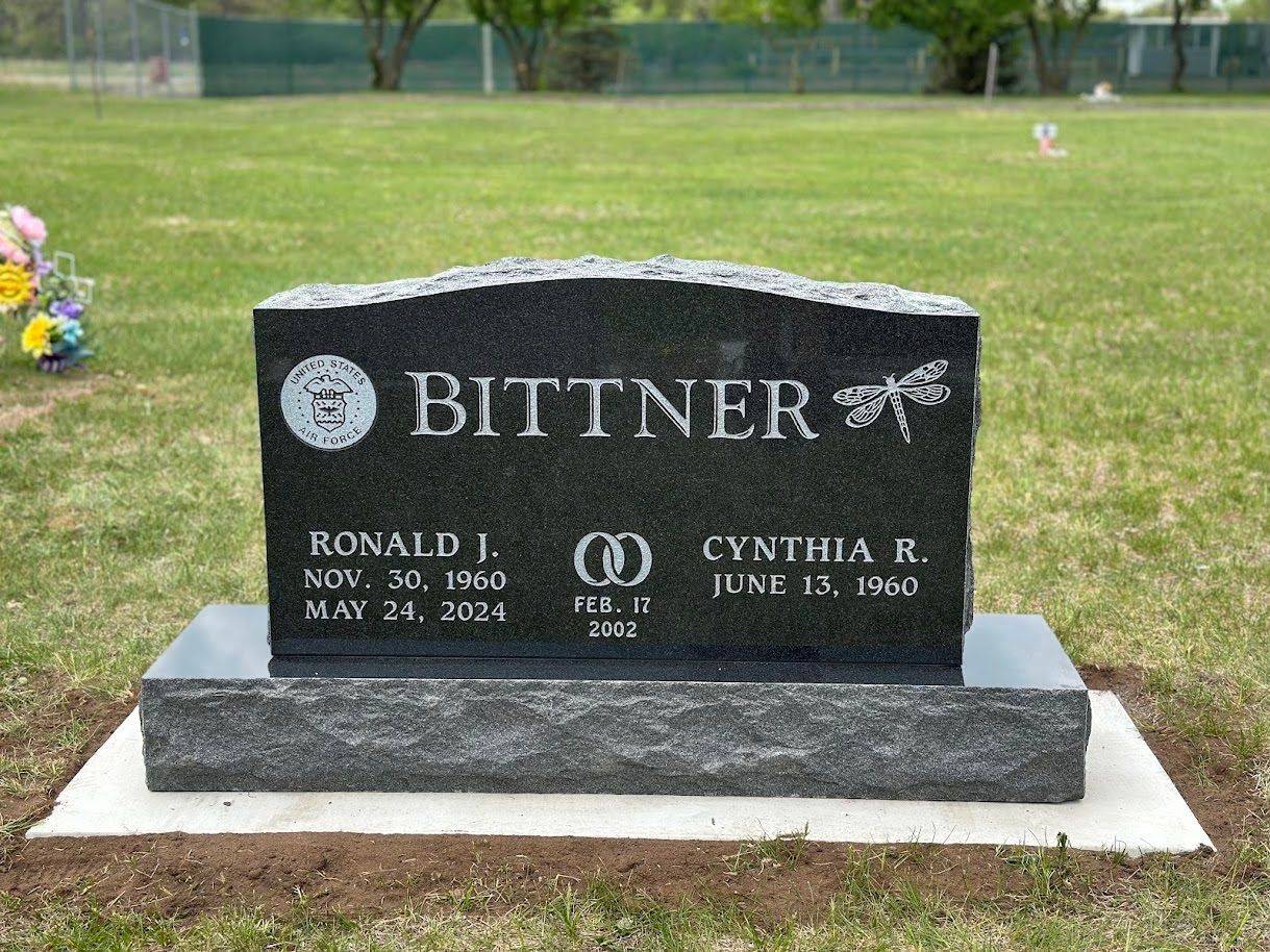 A black granite grave marker for the Bittner family, featuring two names, dates, and a decorative wedding ring emblem.
