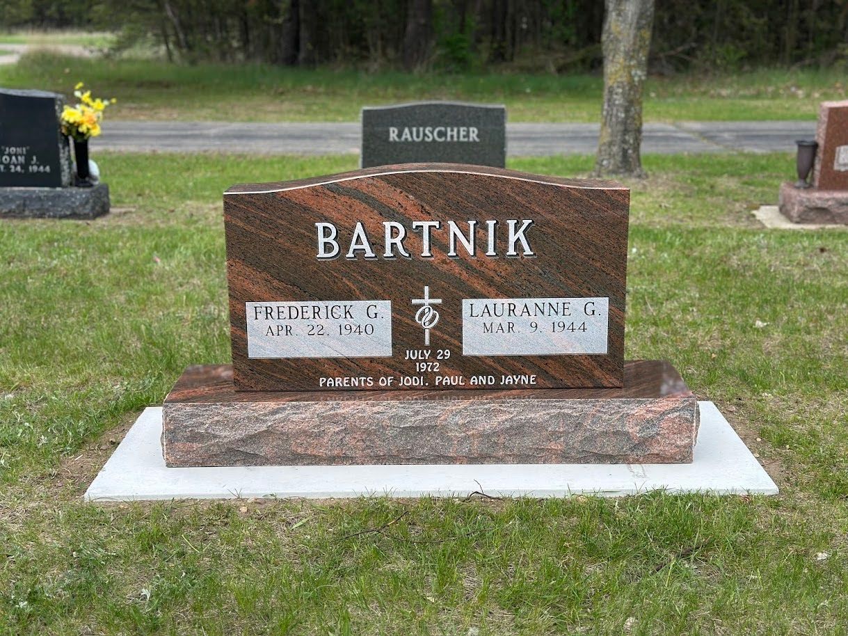 A polished, multi-colored granite headstone for the Bartnik family, centered in a cemetery with a grassy lawn.