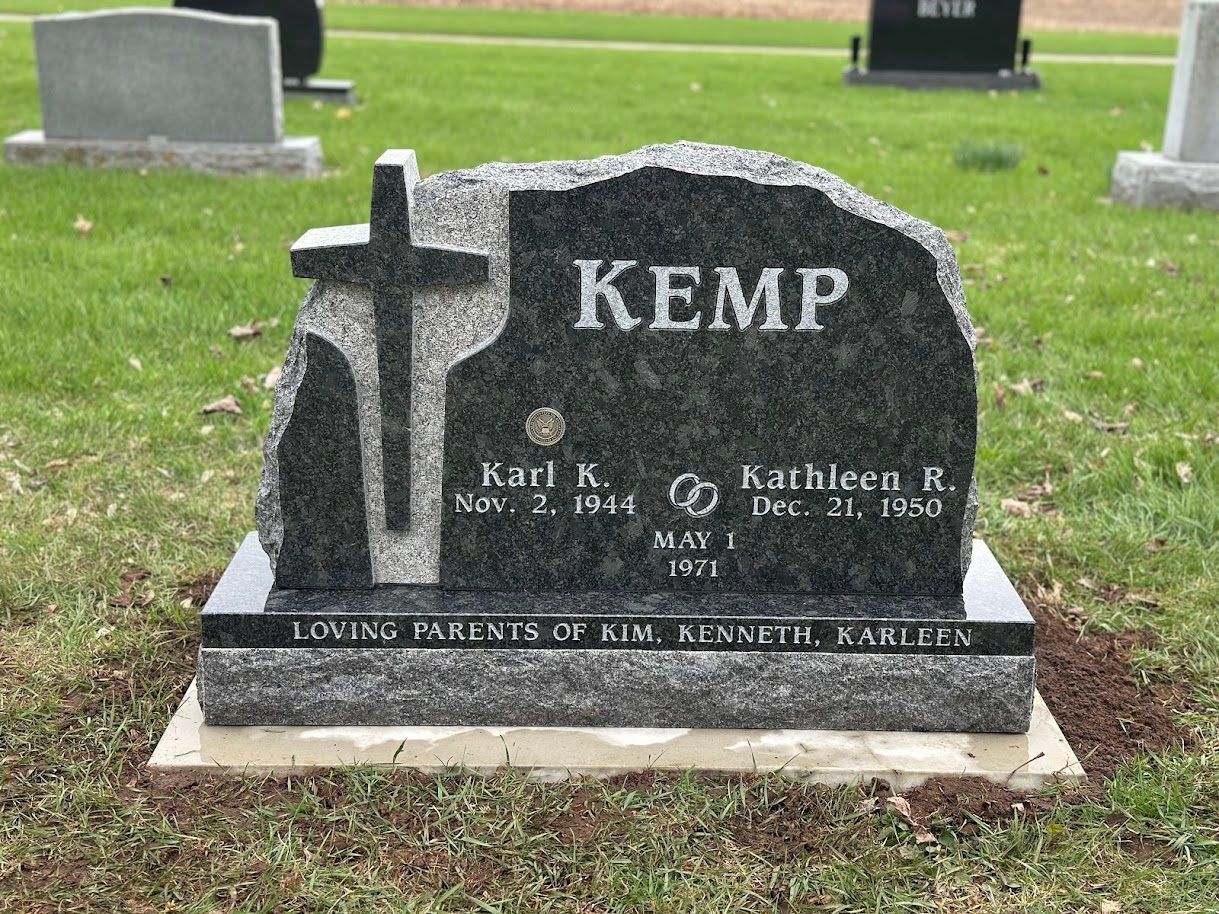 A dark gray granite headstone for the Kemp family, featuring a cross carving and engraved names and dates in a cemetery.