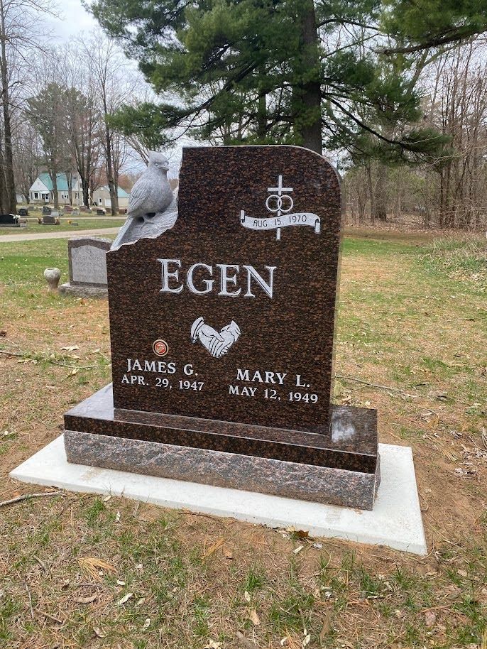 A polished brown granite tombstone for the Egen family, featuring a carved dove, engraved cross, and names in a cemetery.