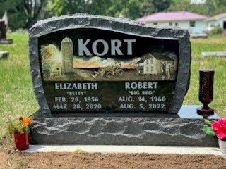 A granite gravestone for Elizabeth and Robert Kort, featuring an etched farm scene and their names and dates.