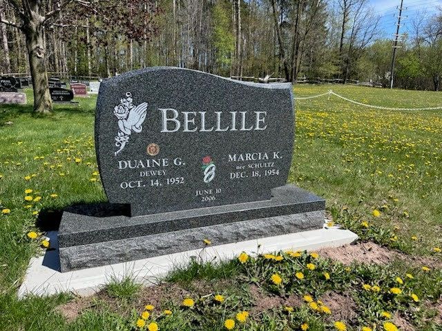 A dark grey, upright granite gravestone for the Bellile family, centered in a grassy cemetery field with yellow flowers.