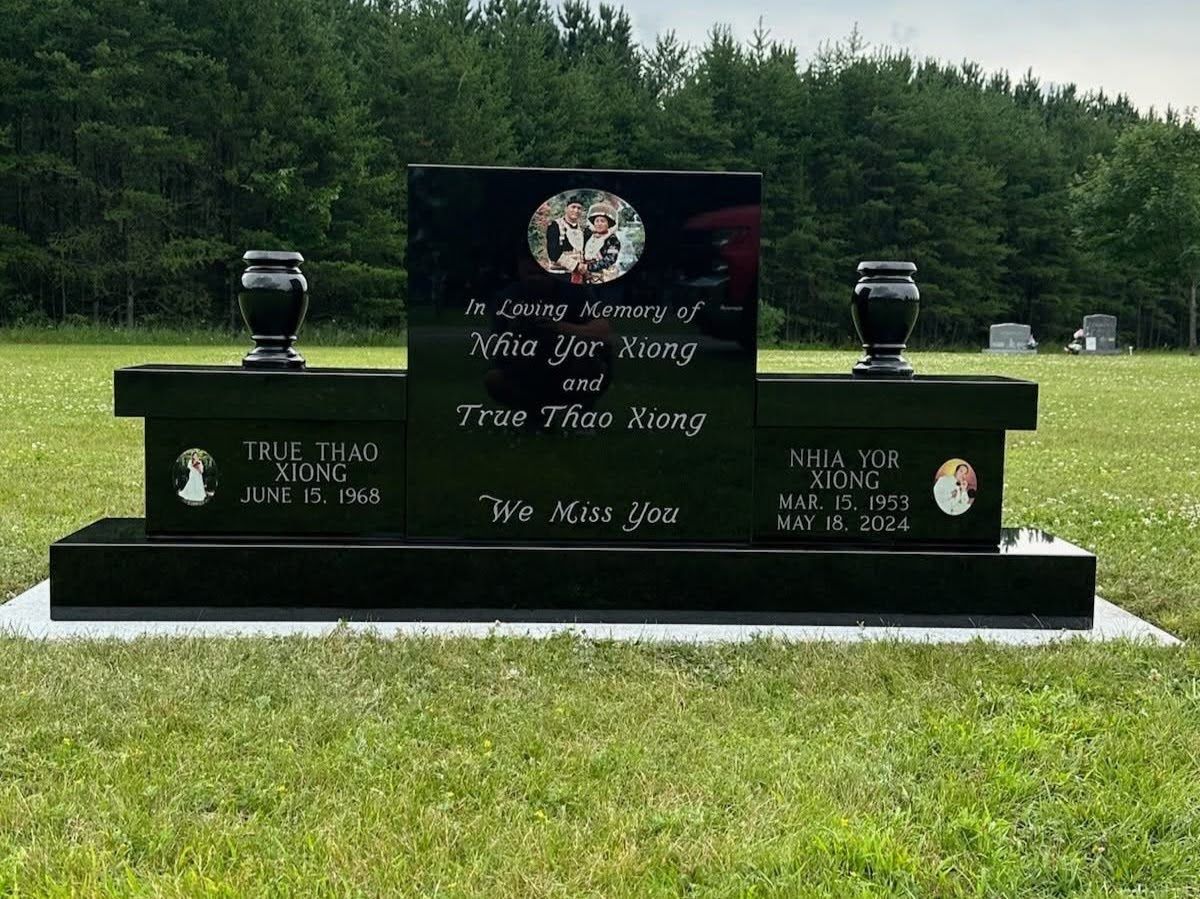 A black granite memorial headstone with two vases in a grassy field against a backdrop of trees.