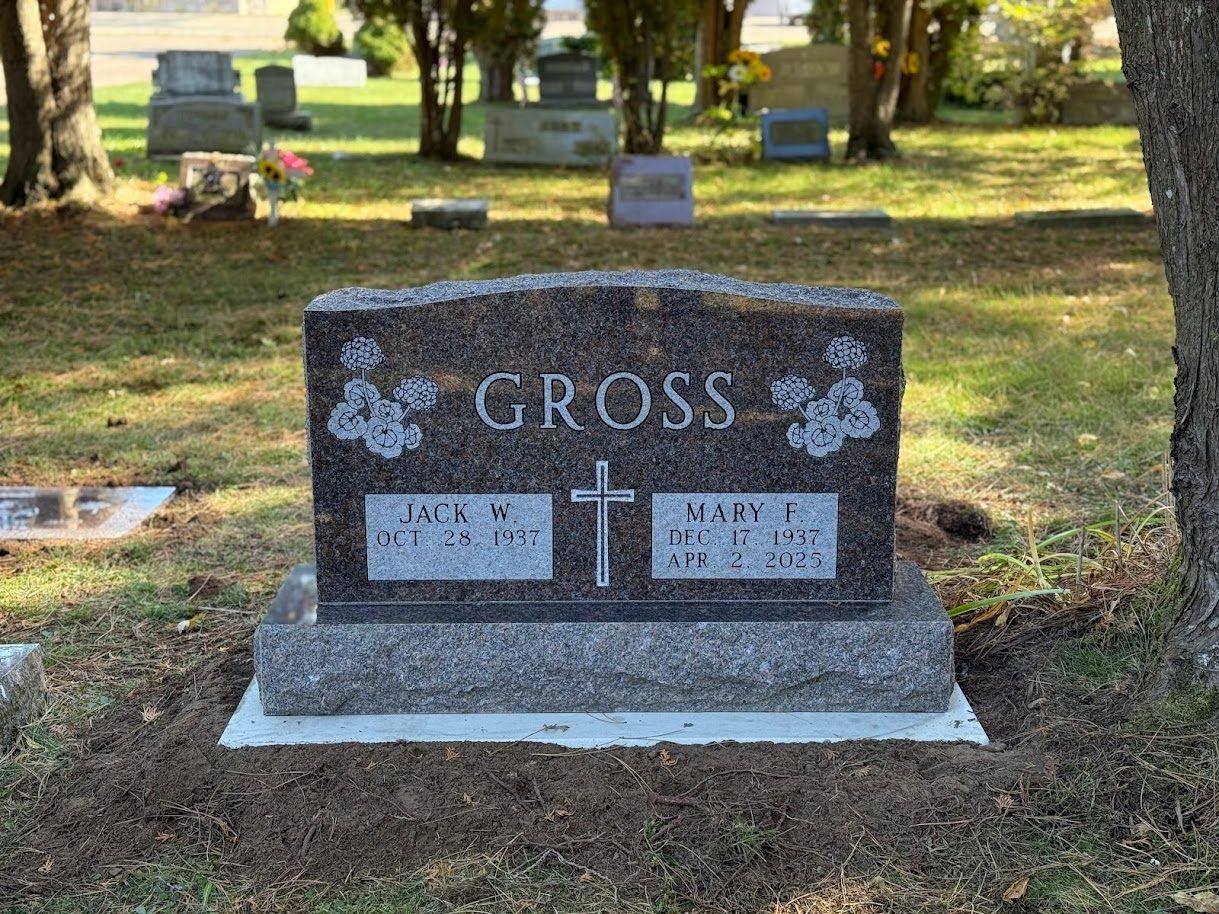 A brown granite gravestone for the Gross family with a central cross, located in a cemetery on a sunny day.
