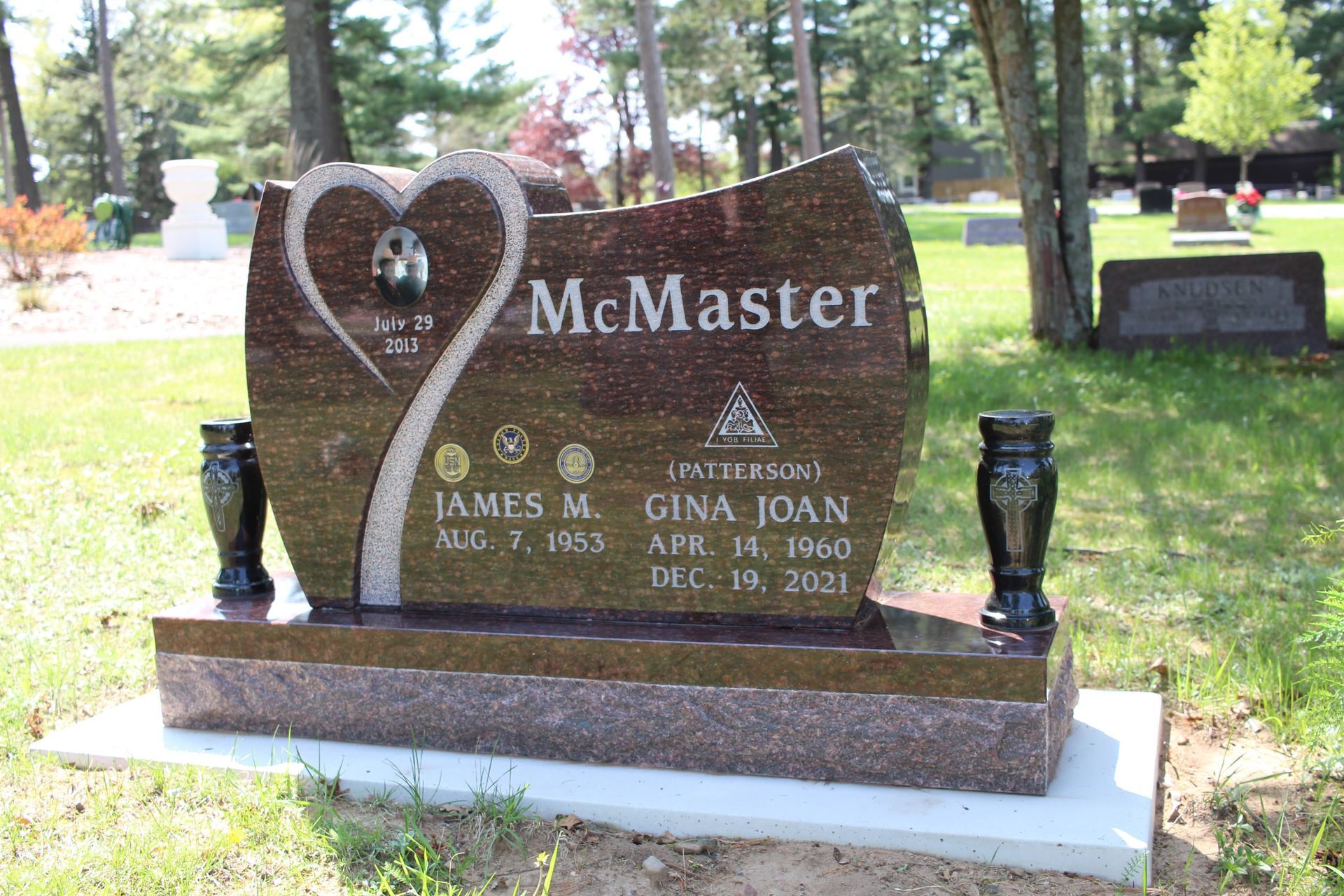 A reddish-brown granite headstone for the McMaster family, featuring a heart-shaped etching and a circular portrait.
