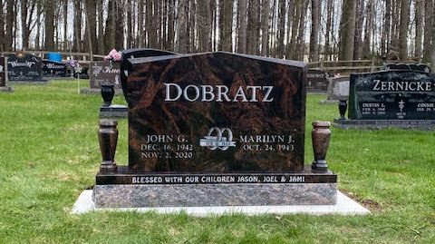 A polished brown and black granite headstone with the name DOBRATZ, in a cemetery setting with trees in the background.