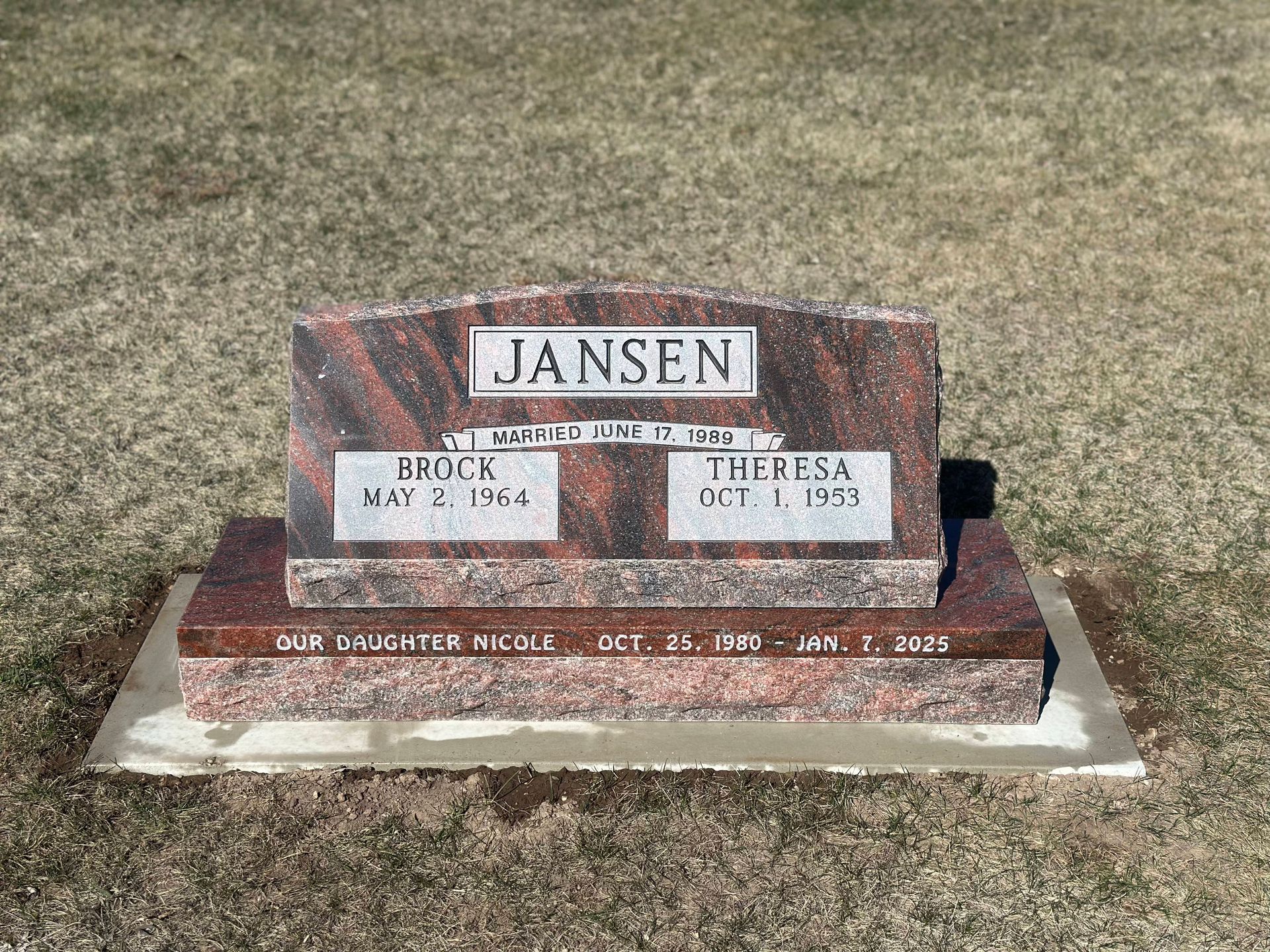 A red granite double headstone for the Jansen family, with names and dates inscribed, set in a grassy cemetery.