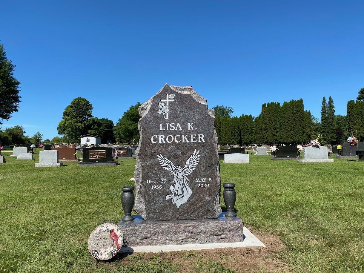 A dark granite headstone in a sunny cemetery, engraved with the name 