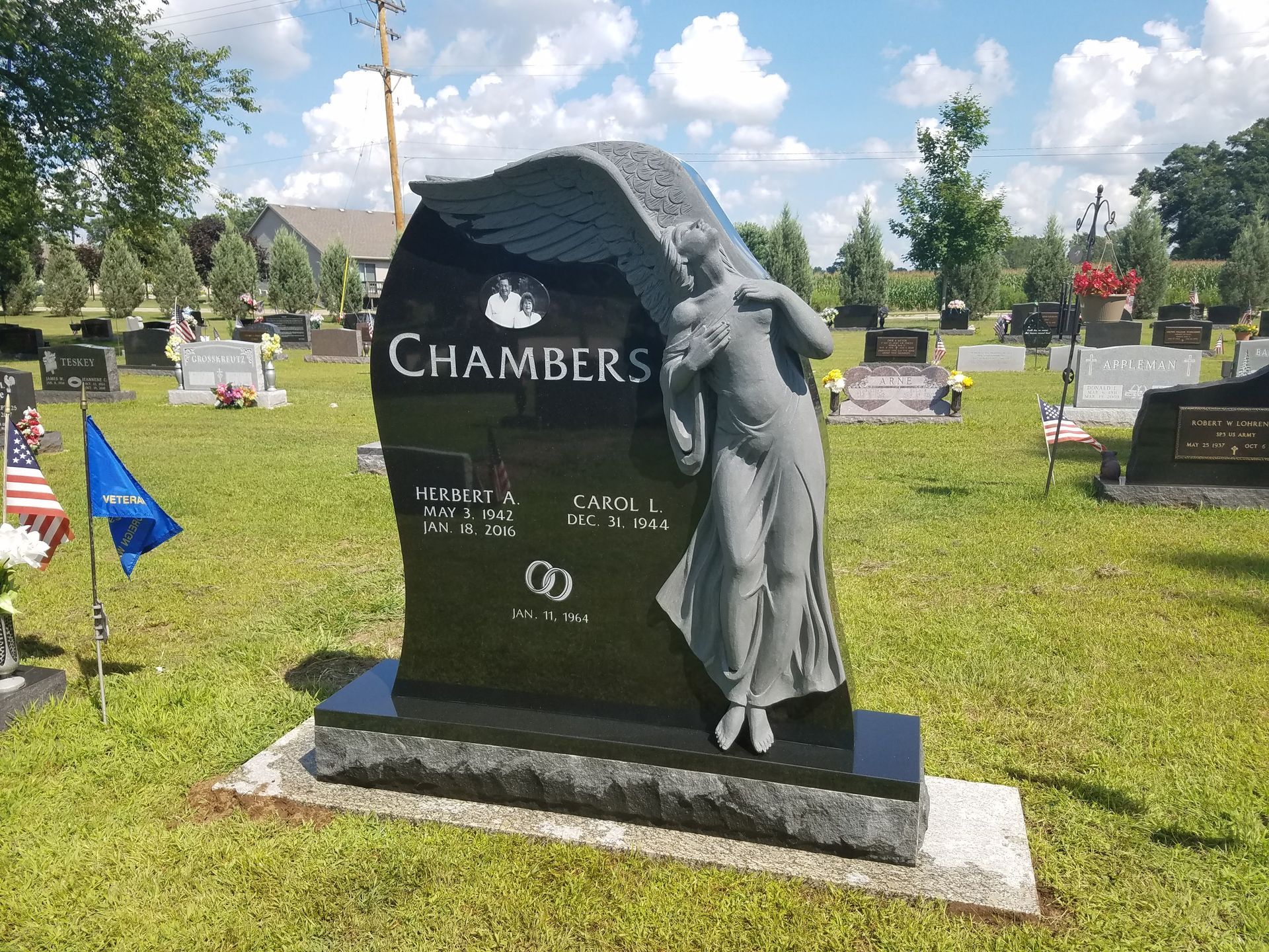 A black granite cemetery monument for the Chambers family, featuring an angel carving, in a sunny, grass-covered cemetery.