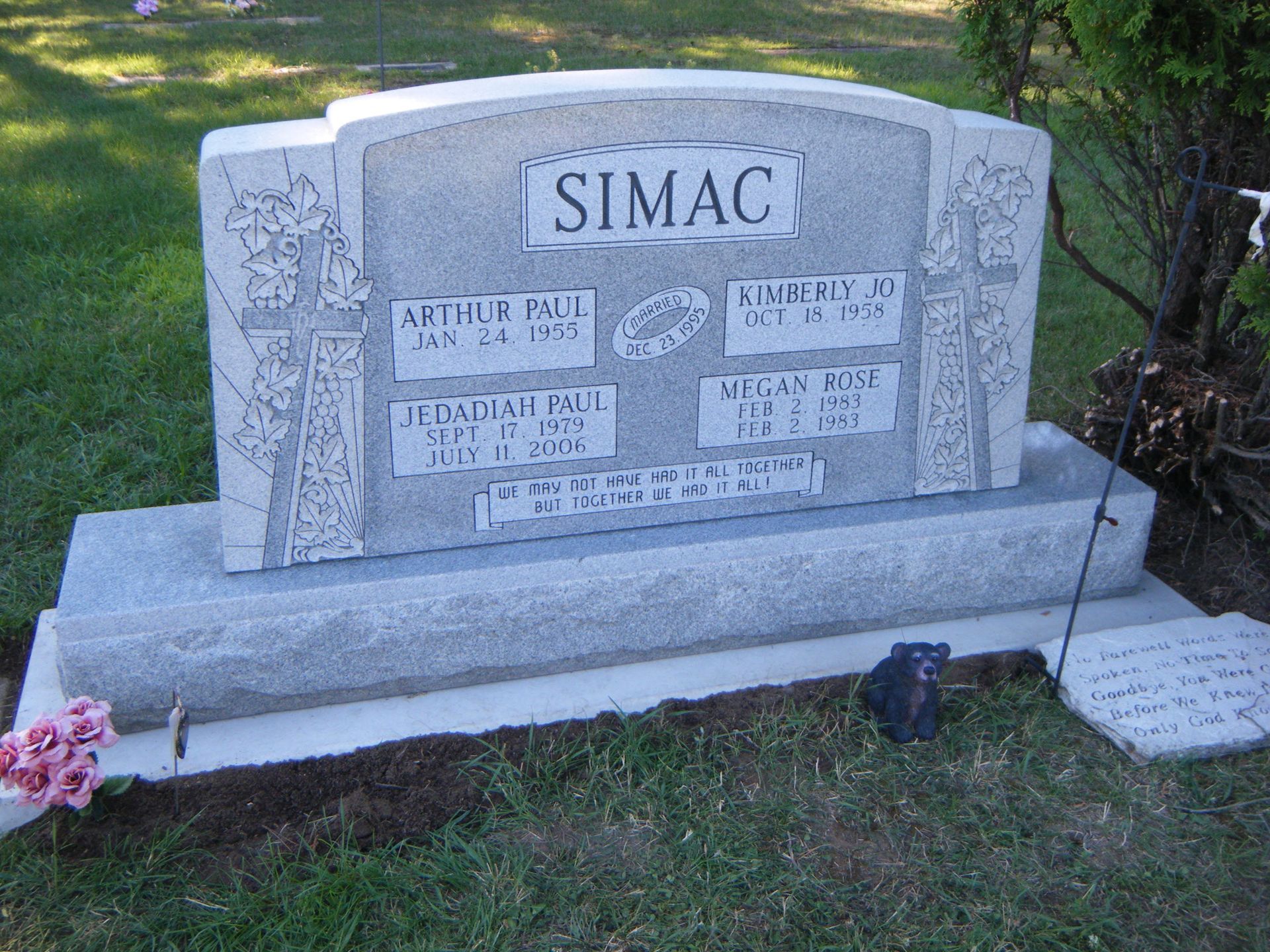 A gray granite gravestone for the Simac family, featuring four names and dates, set in a grassy cemetery.