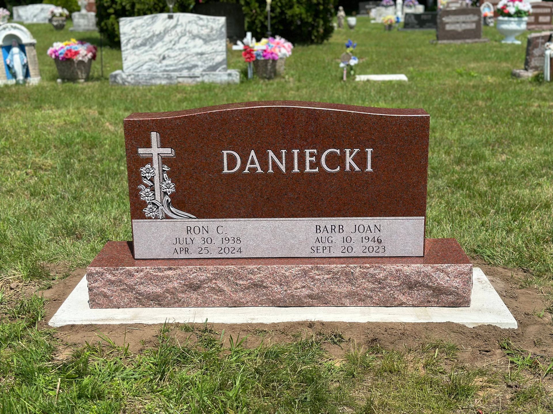 A red granite gravestone with a cross engraving, inscribed with 