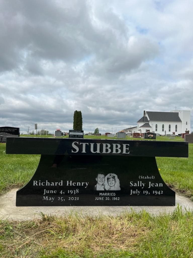 A black bench is sitting in the middle of a grassy field in a cemetery.