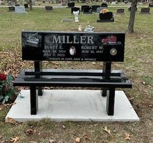 A black bench is sitting in a cemetery next to a grave.