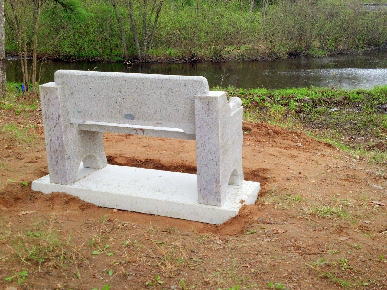 A stone bench is sitting in the dirt next to a river.