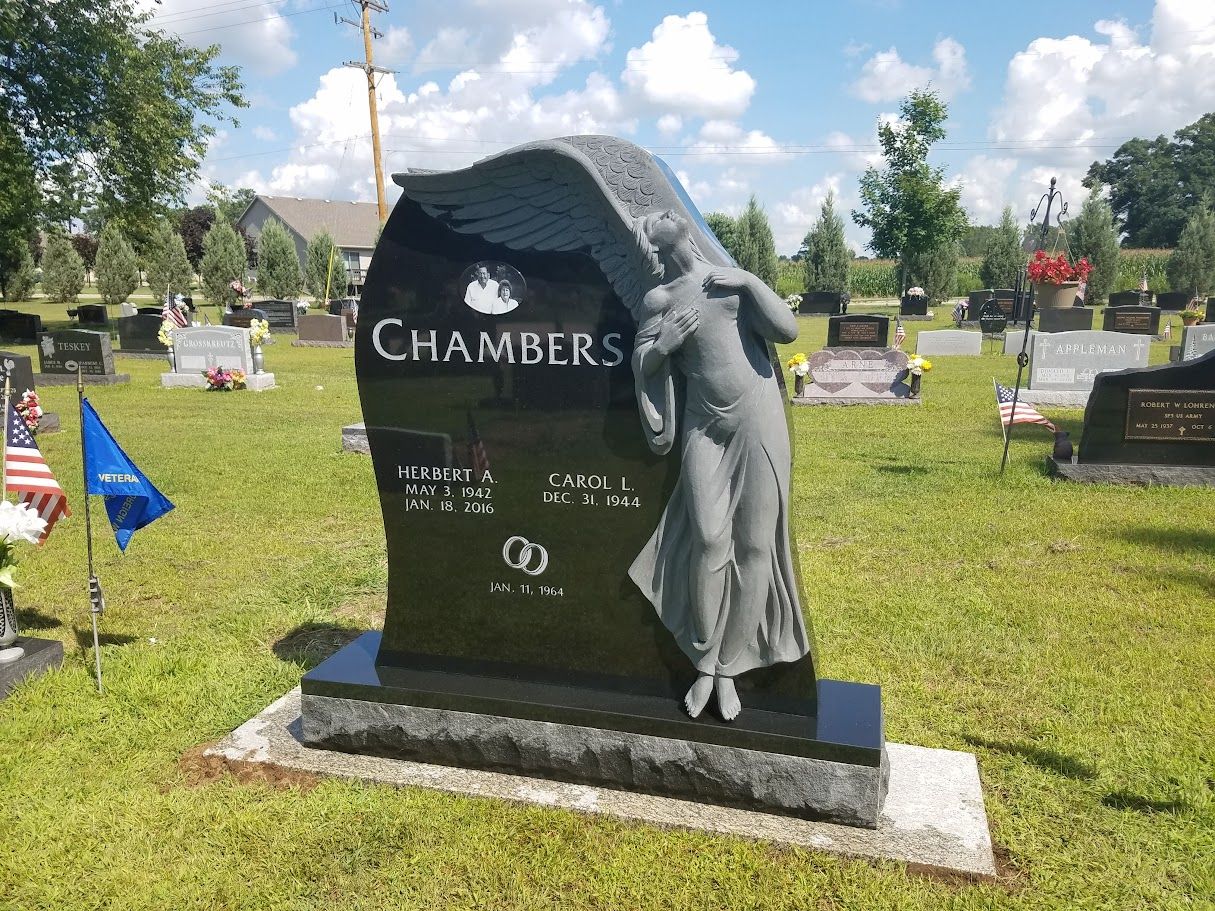 A black gravestone with a statue of a woman in a cemetery.