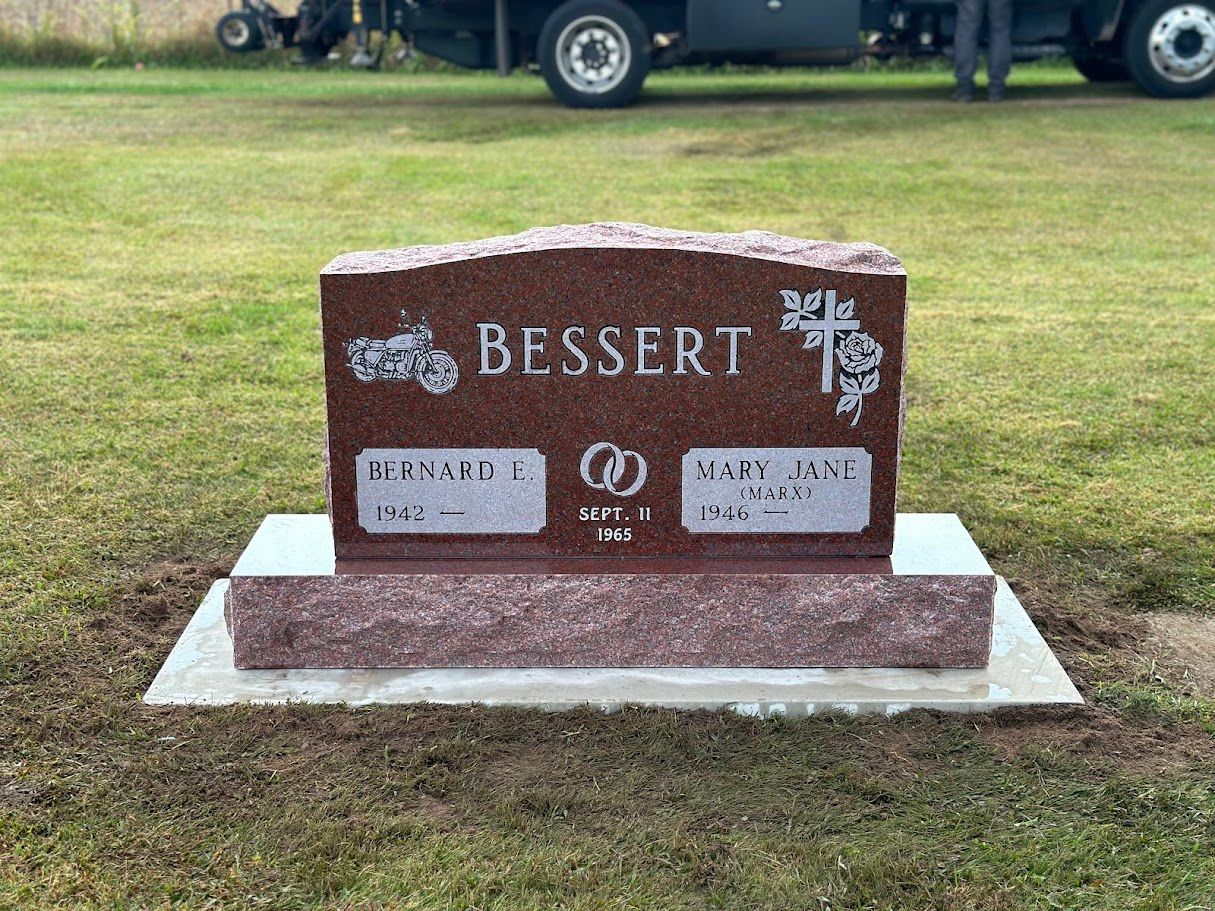A gravestone in a cemetery with a truck parked in the background.