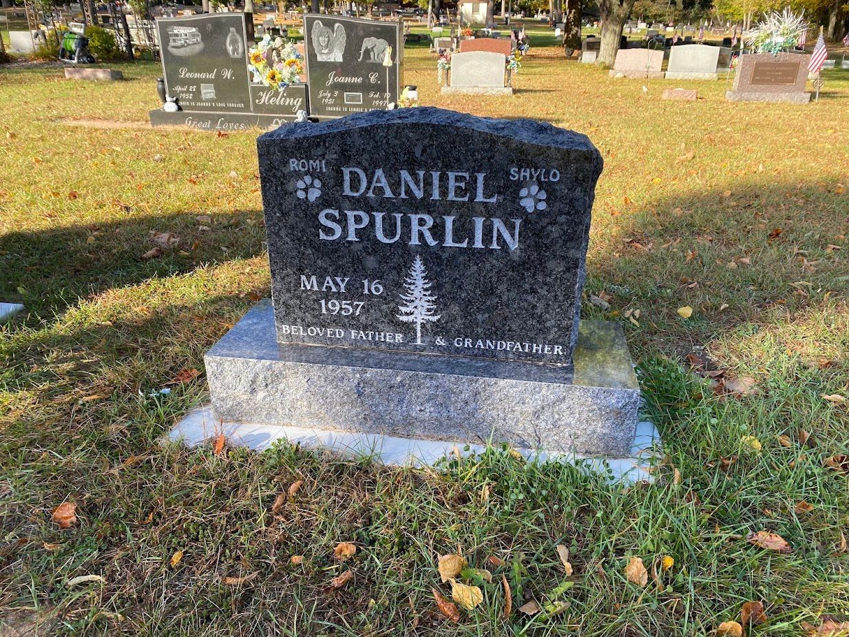 A black gravestone in a cemetery with a name written on it.