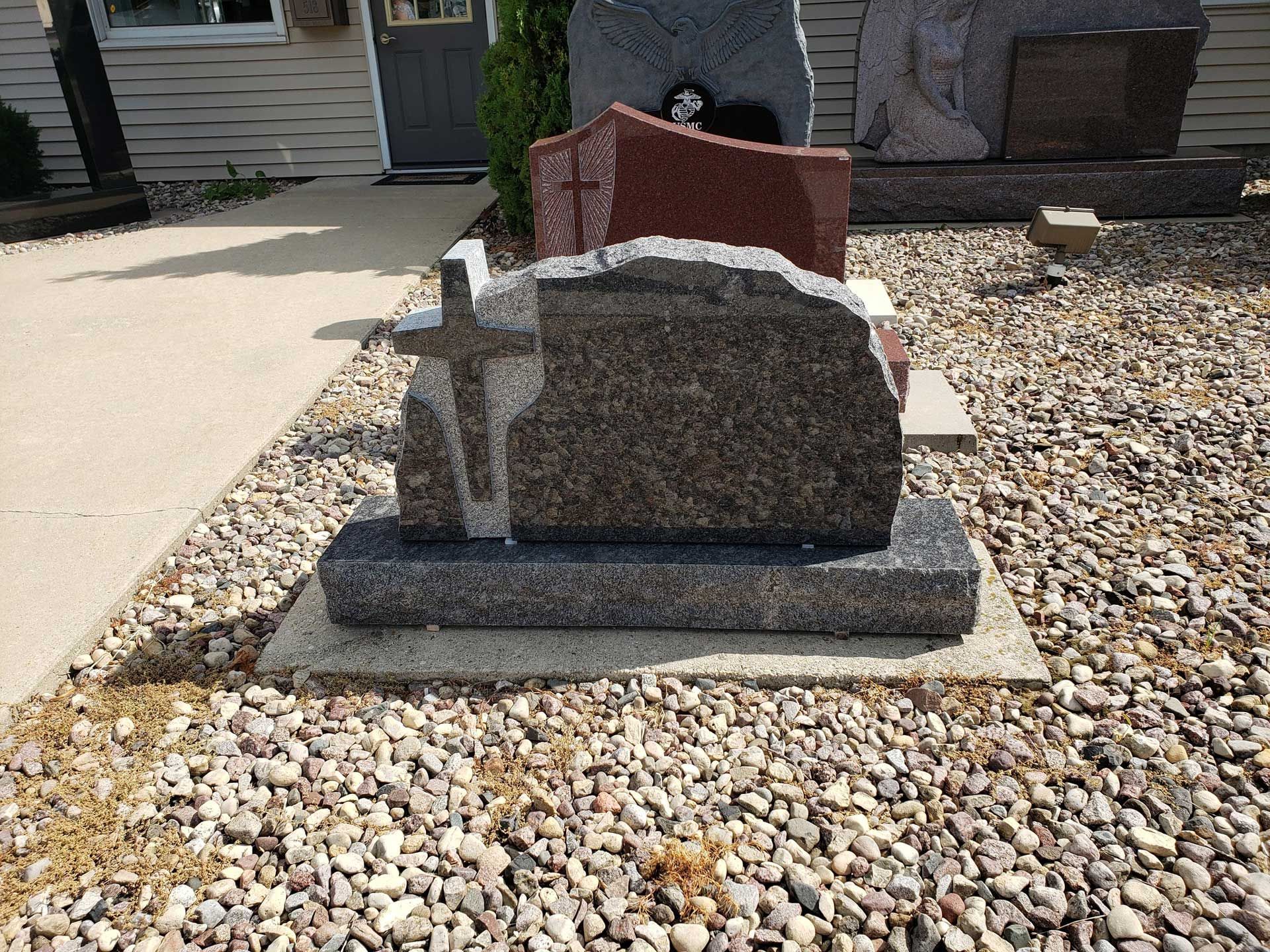 A gravestone with a cross on it is sitting on top of a pile of gravel.