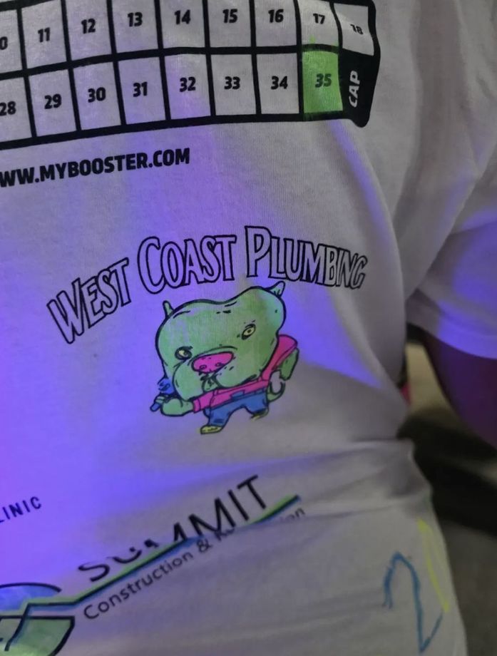 Person wearing a white shirt with a colorful “West Coast Plumbing” bear logo and sponsor text.
