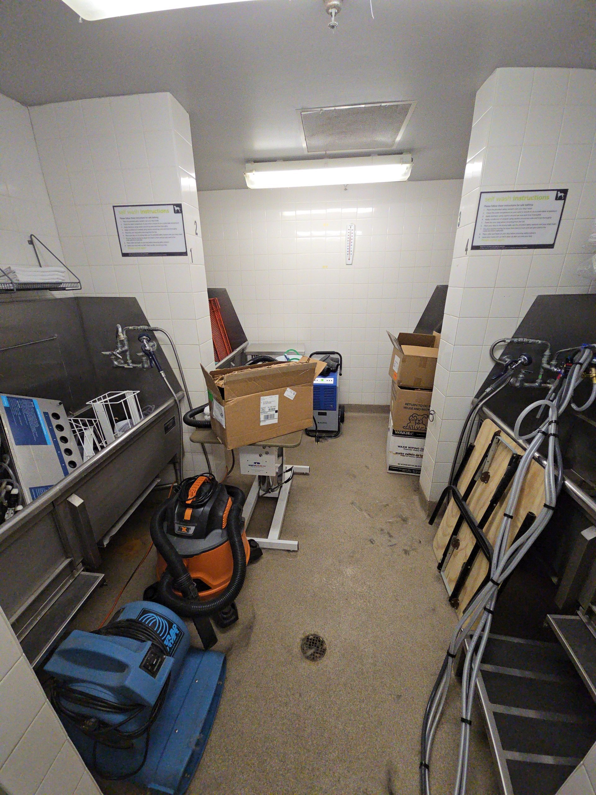 Narrow storage room with shelves of tools, boxes, and equipment on both sides.