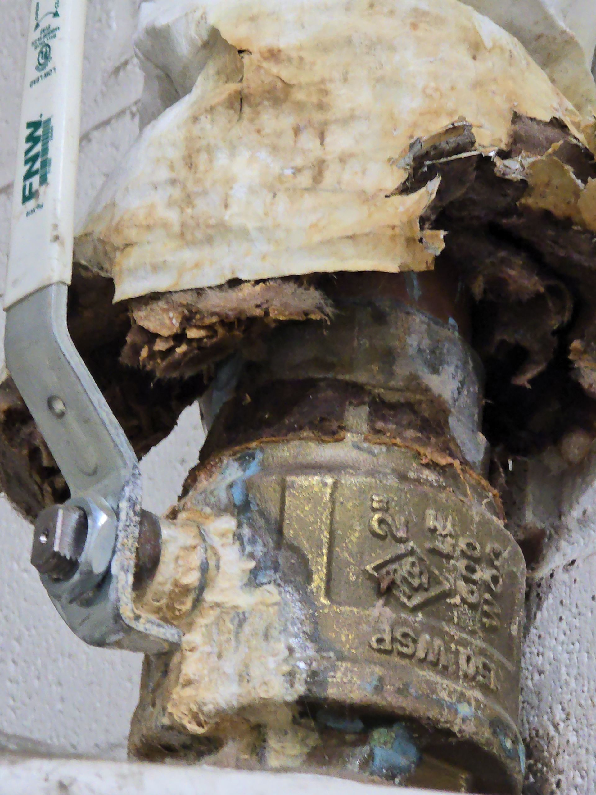 Corroded brass plumbing valve with severe water damage and peeling insulation