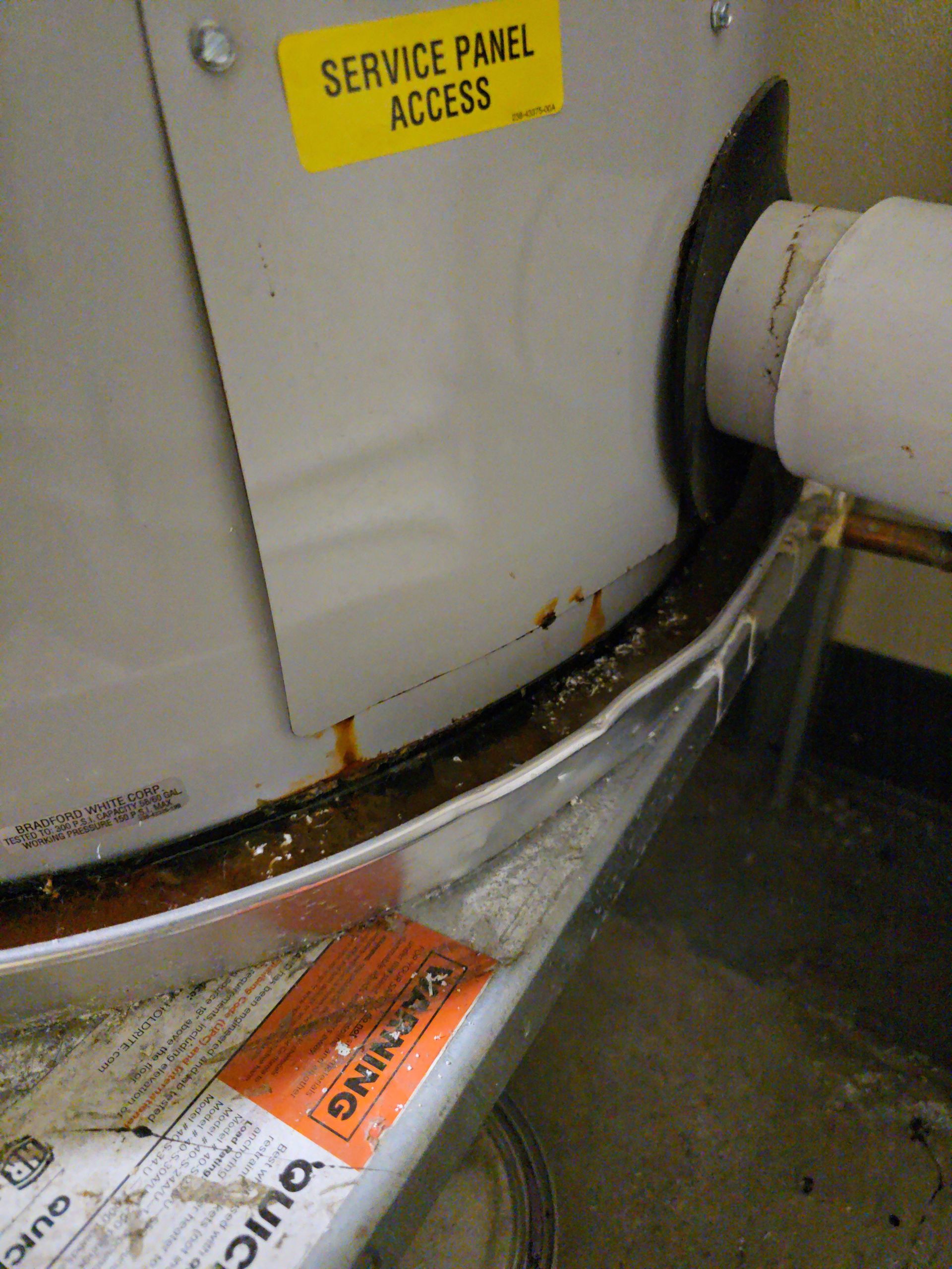 White service panel with yellow label, a bent metal edge, and a pipe in a utility area.