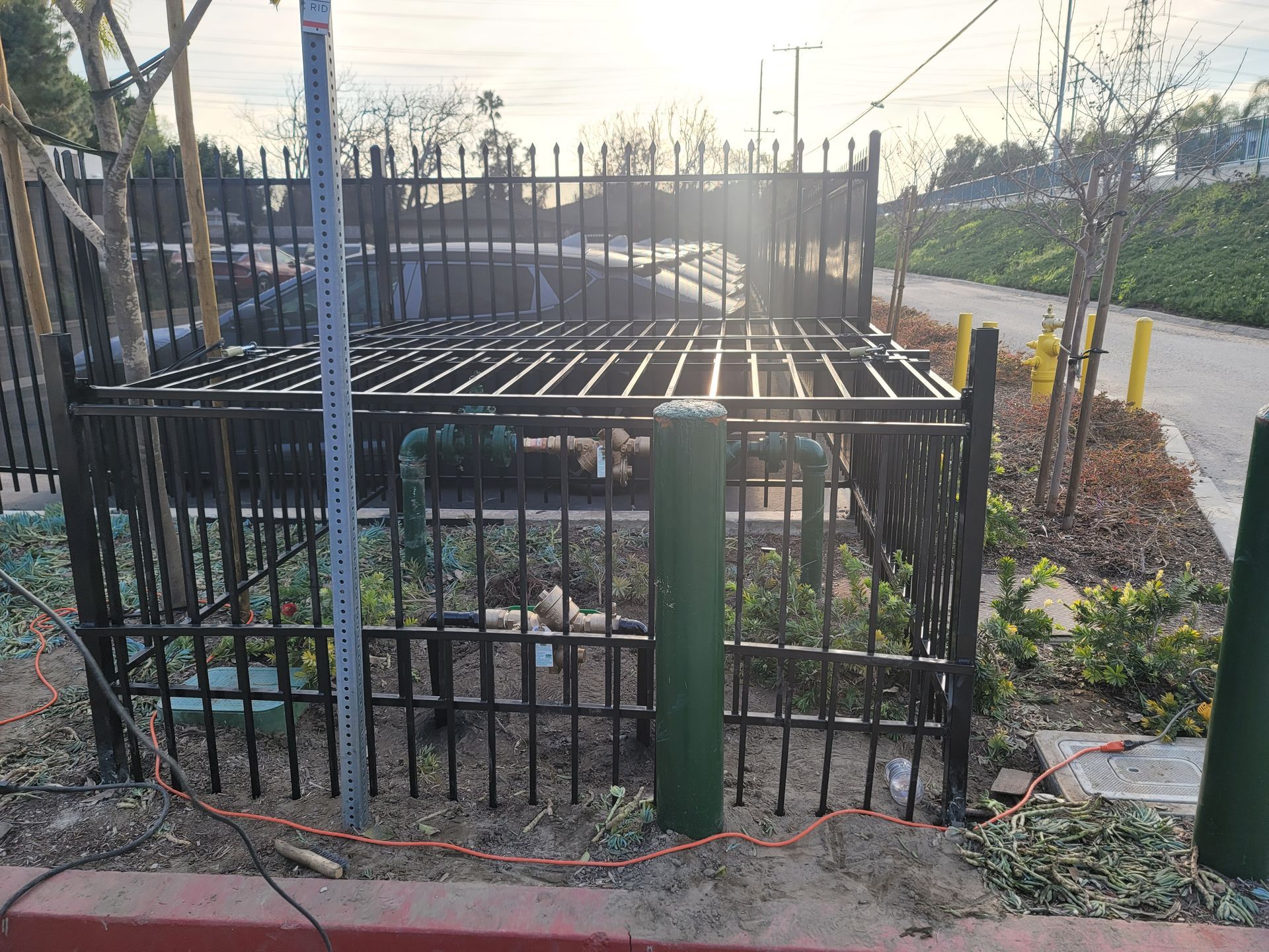Black metal utility enclosure by a roadside, with green posts and fencing in bright sunlight.