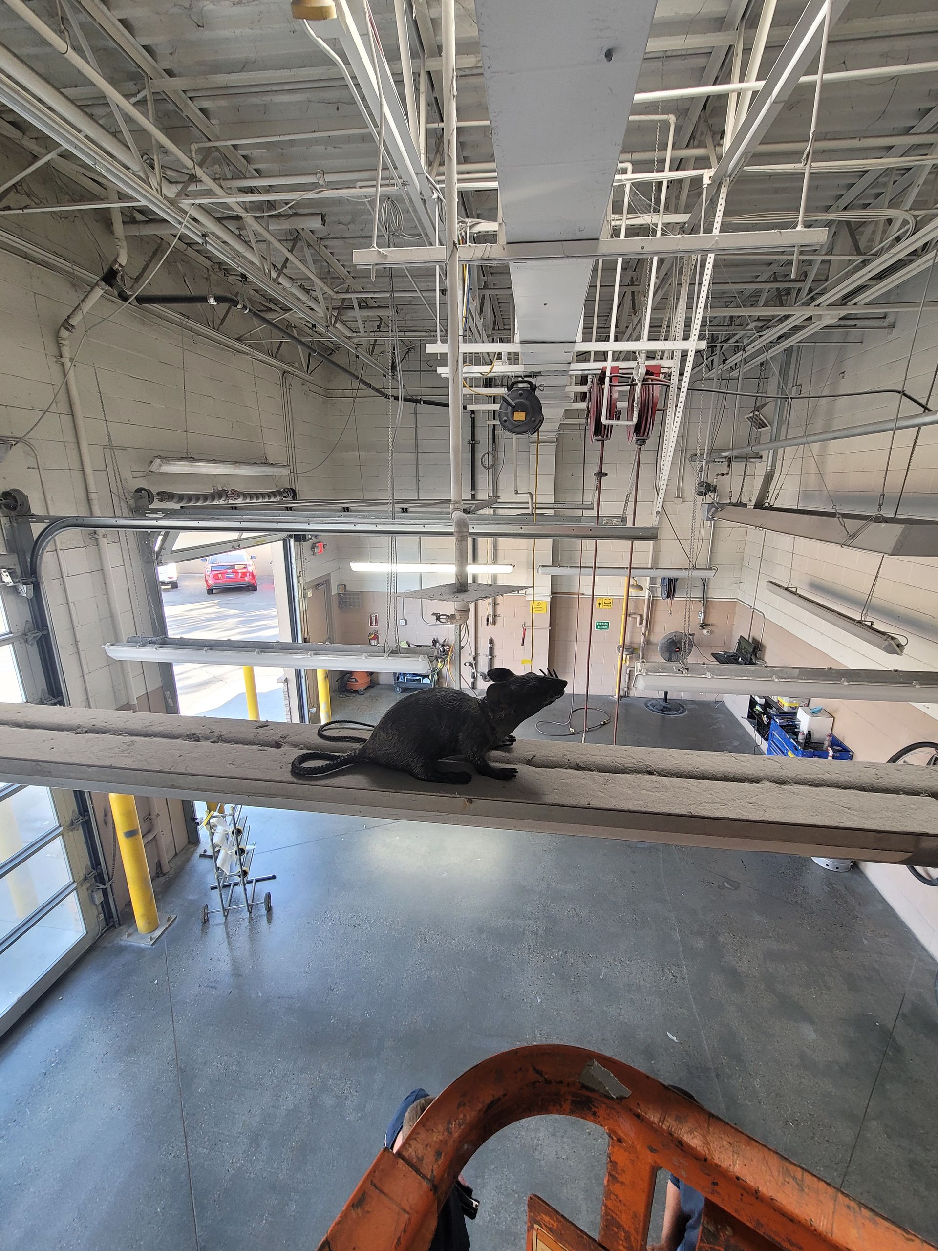 Interior of an industrial facility with overhead cranes, hanging equipment, and a worker below on the floor.