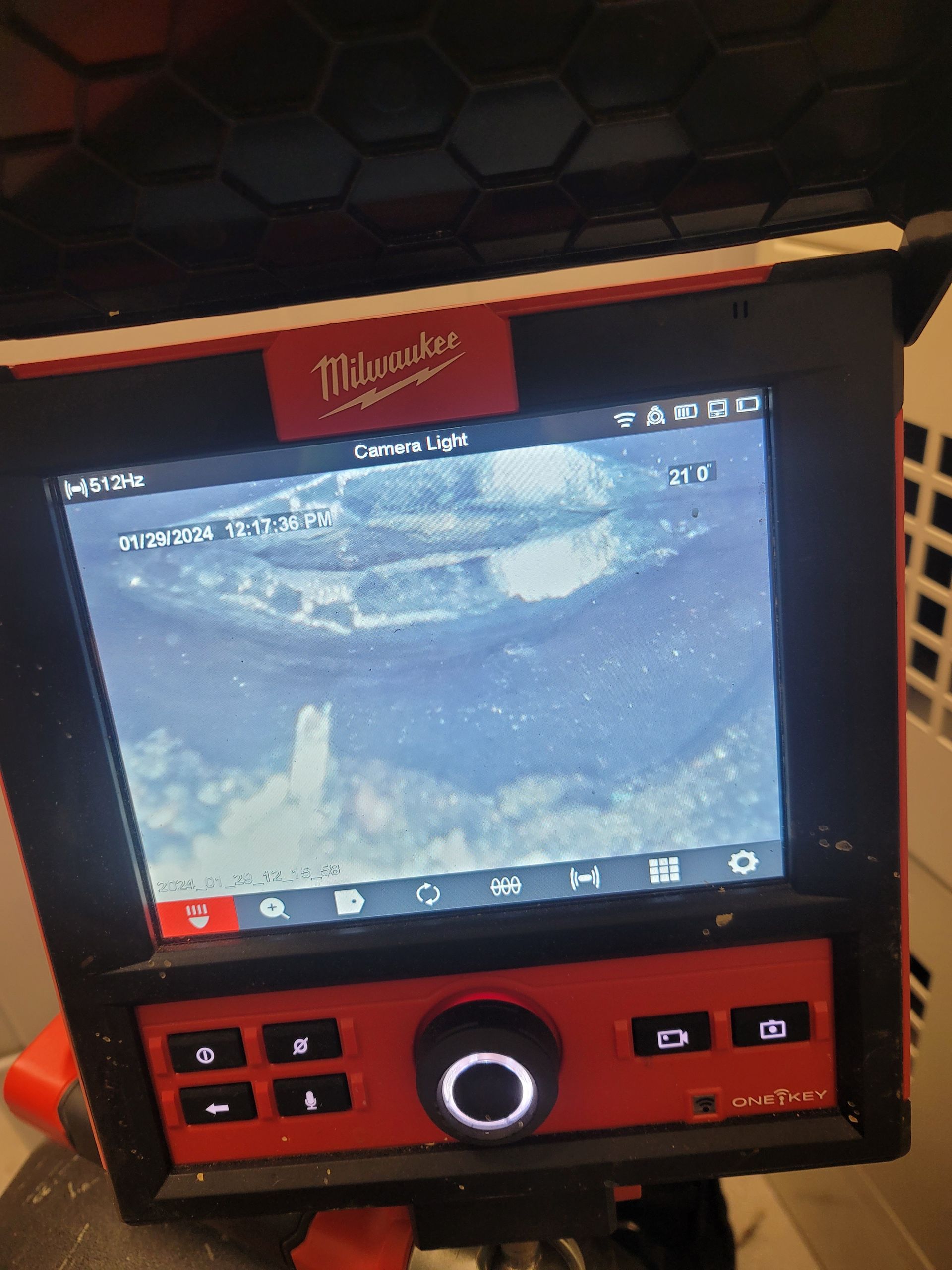 Milwaukee-branded device showing a grainy live camera view, with control buttons and a central dial