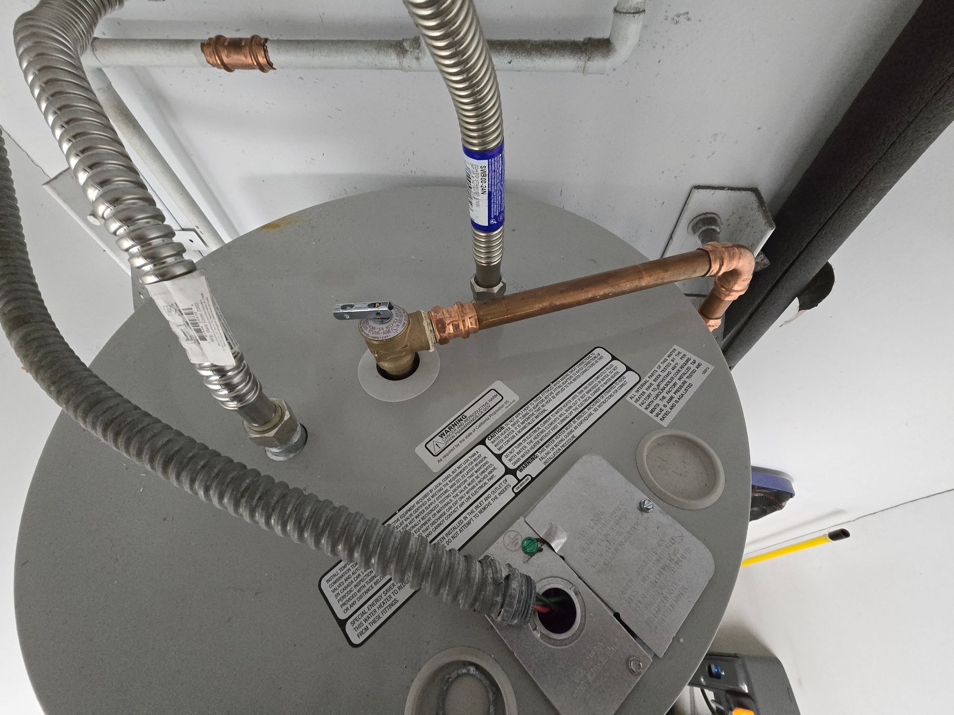 Water heater top with copper and flexible hoses connected to gray tank in a utility area