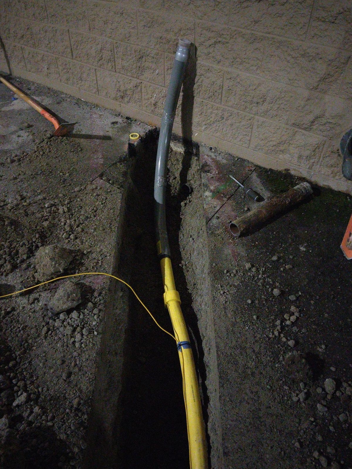 Trench with a yellow cable and gray pipe extending from a hole in a concrete floor