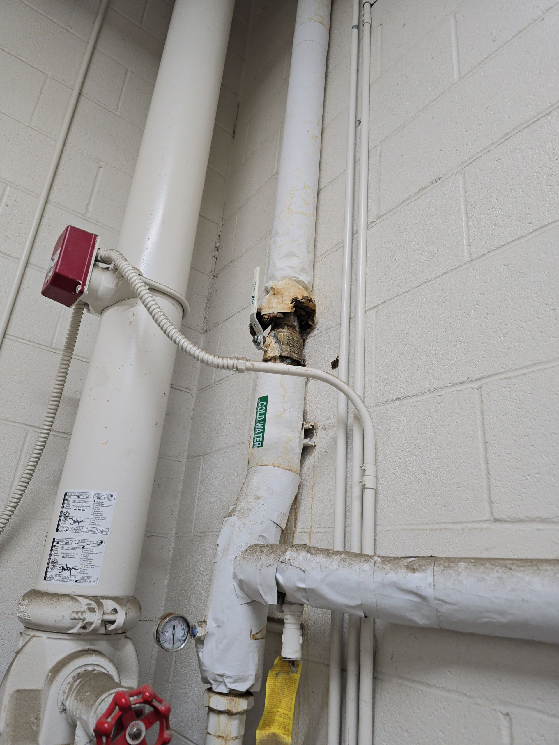 Damaged white pipe with exposed insulation and a red valve in a utility corner