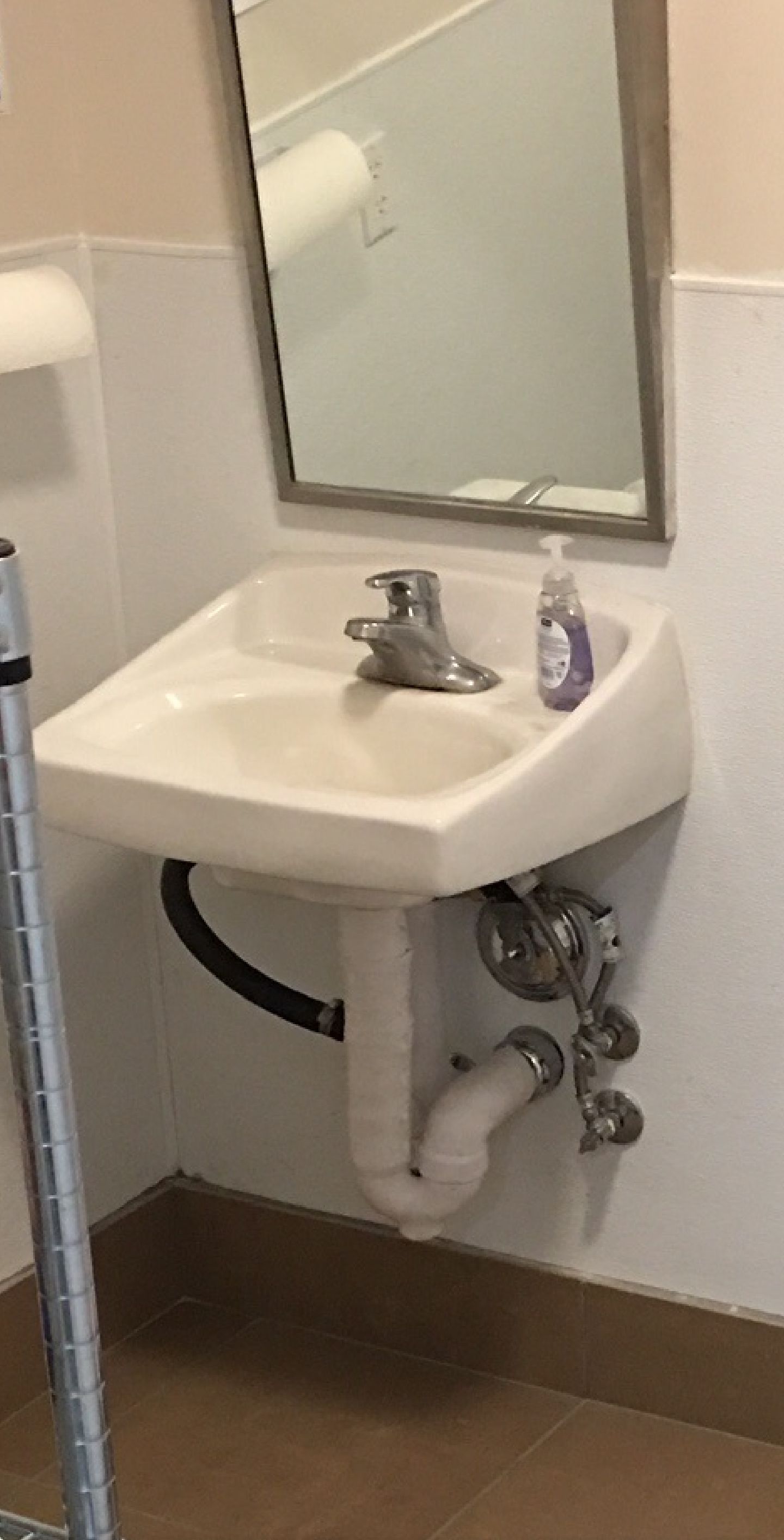 Small wall-mounted sink with mirror and soap dispenser in a restroom stall.