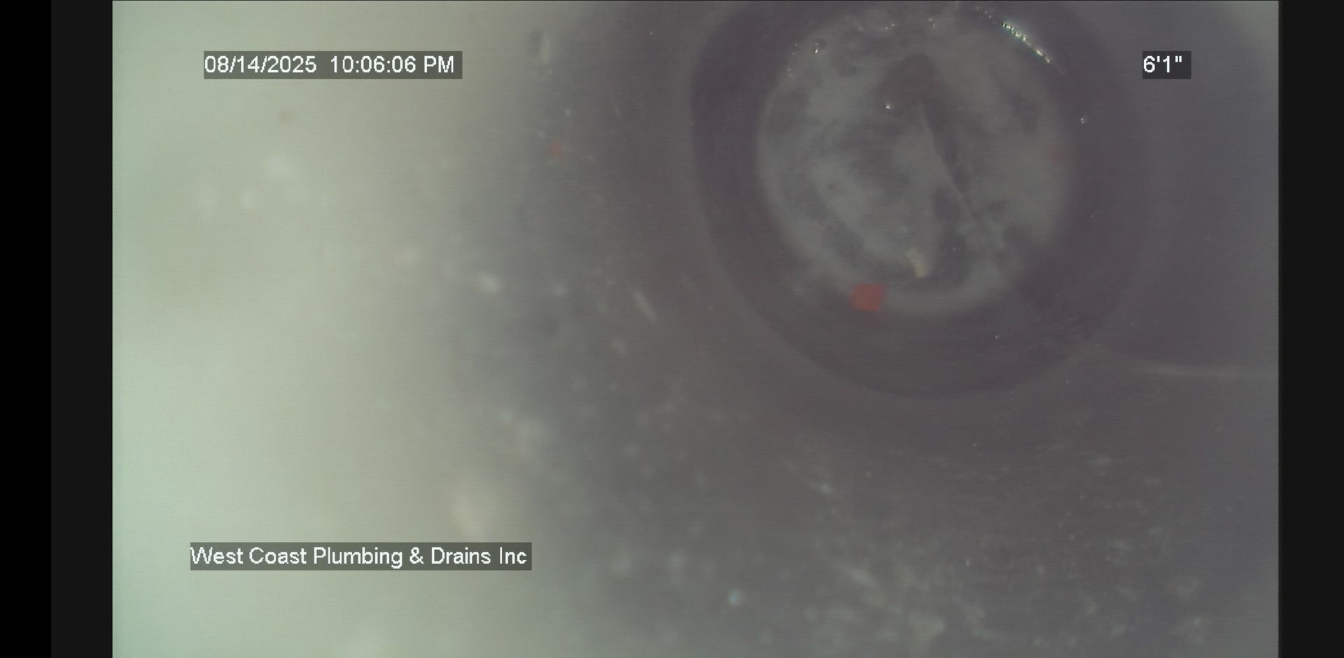 Close-up grainy CCTV view of a circular pipe or drain interior with dim gray walls and a dark center.