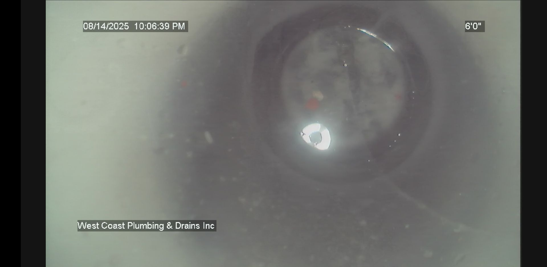 Gray CCTV view of a circular pipe interior with glare and inspection overlays in the corners