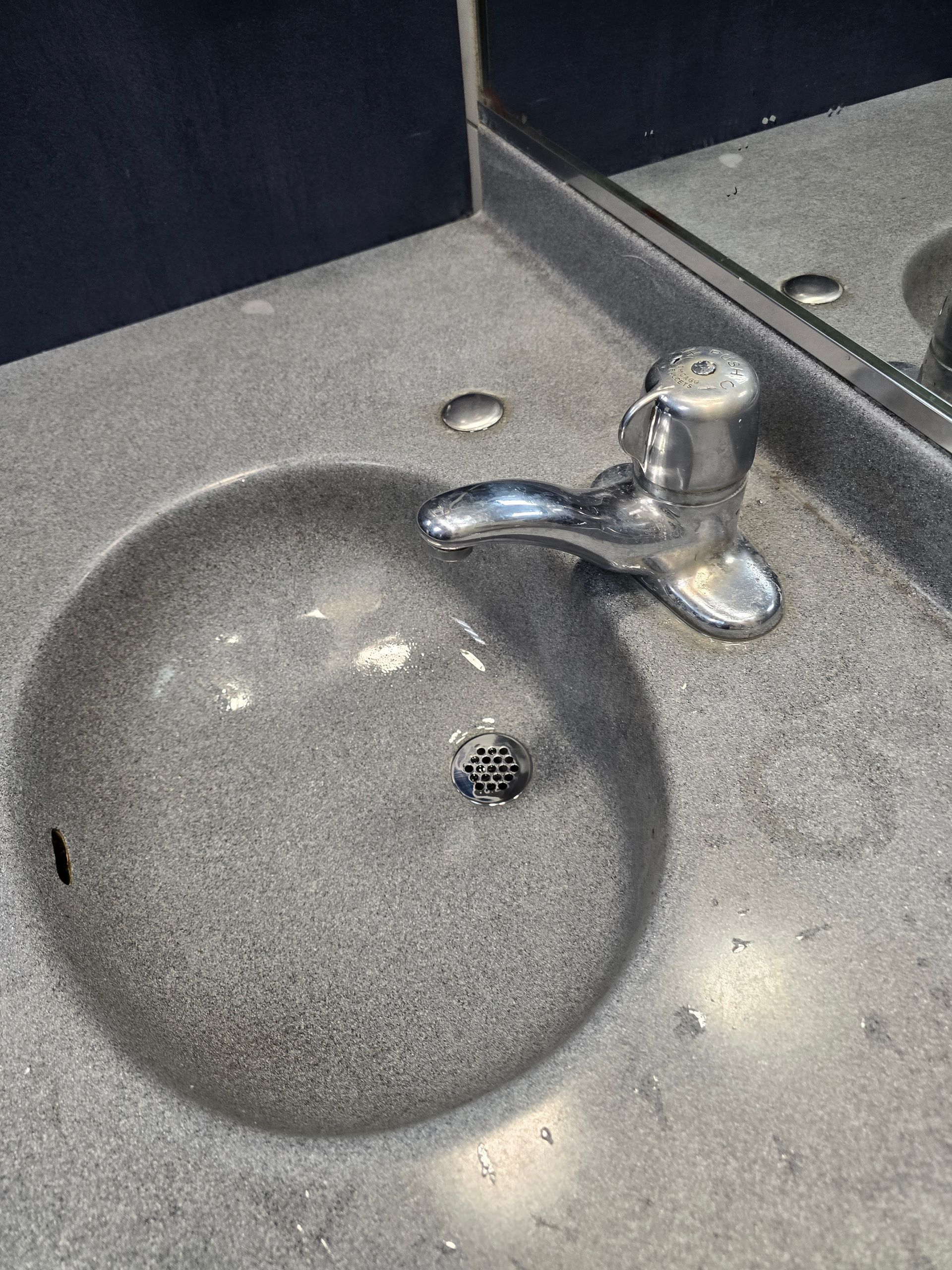 Gray bathroom sink with chrome faucet and a round mirror reflection above the counter