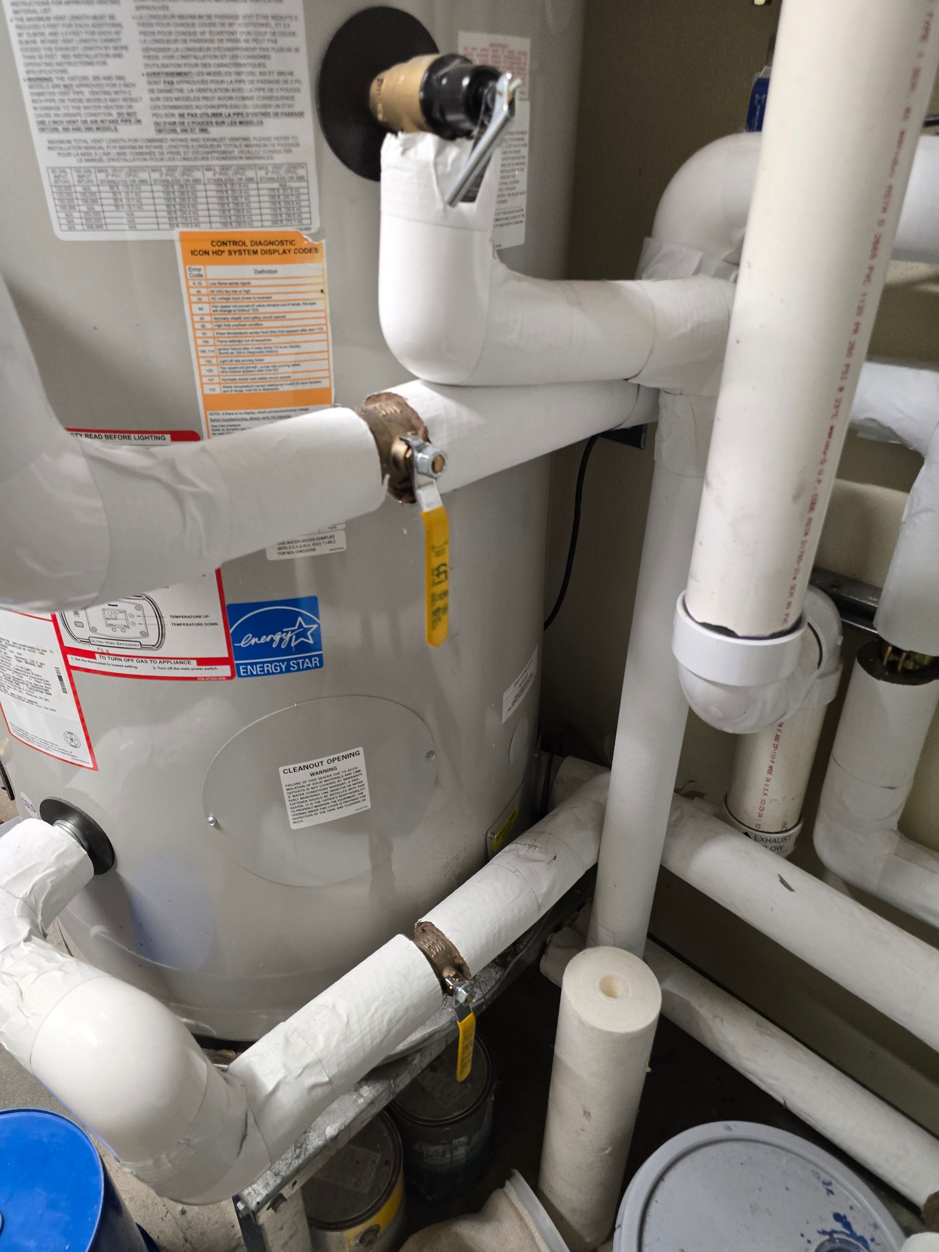 Gray water heater with white pipes and warning labels in a utility closet
