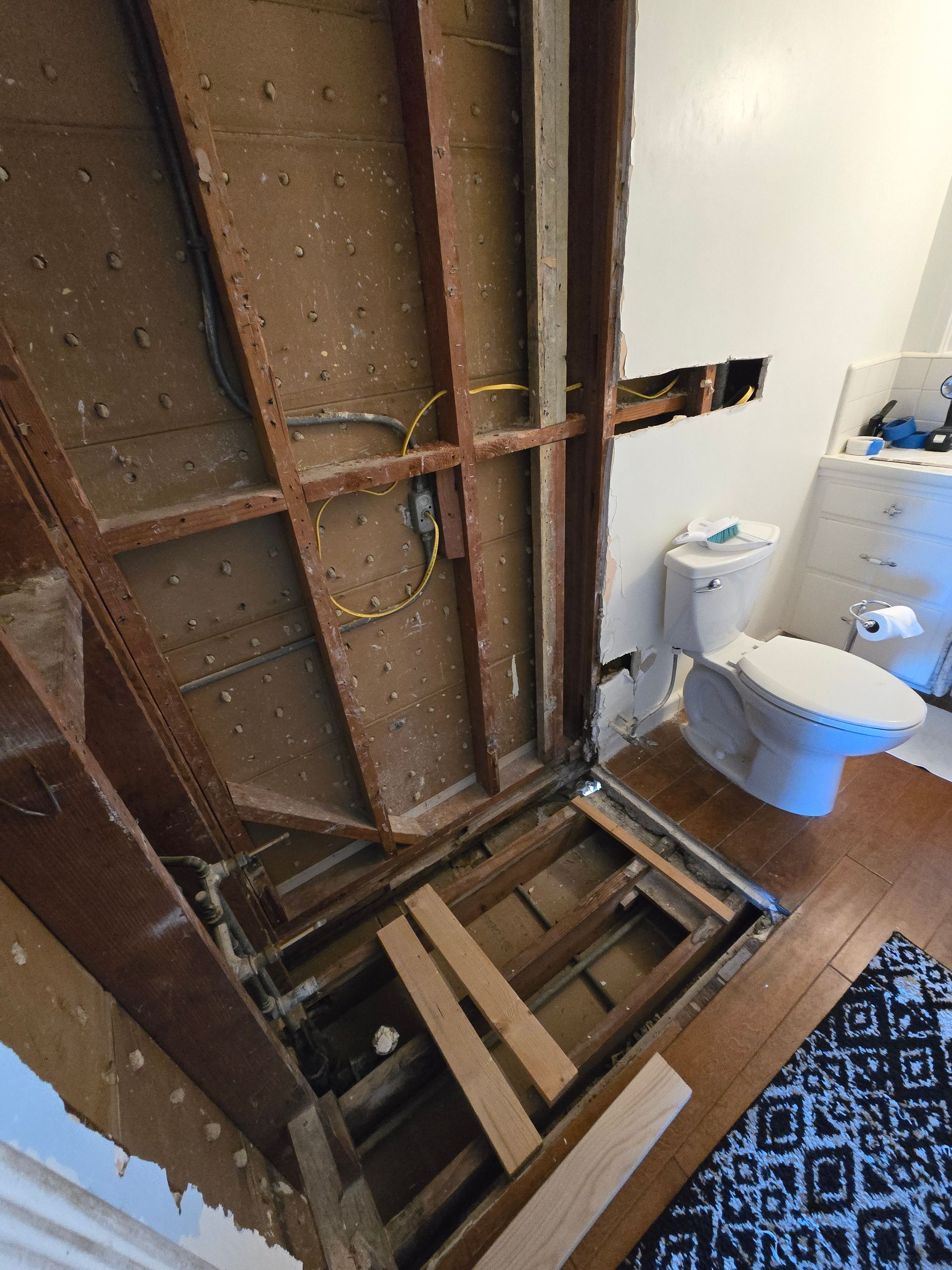 Bathroom under renovation with exposed wall framing, open floor, toilet, and sink visible