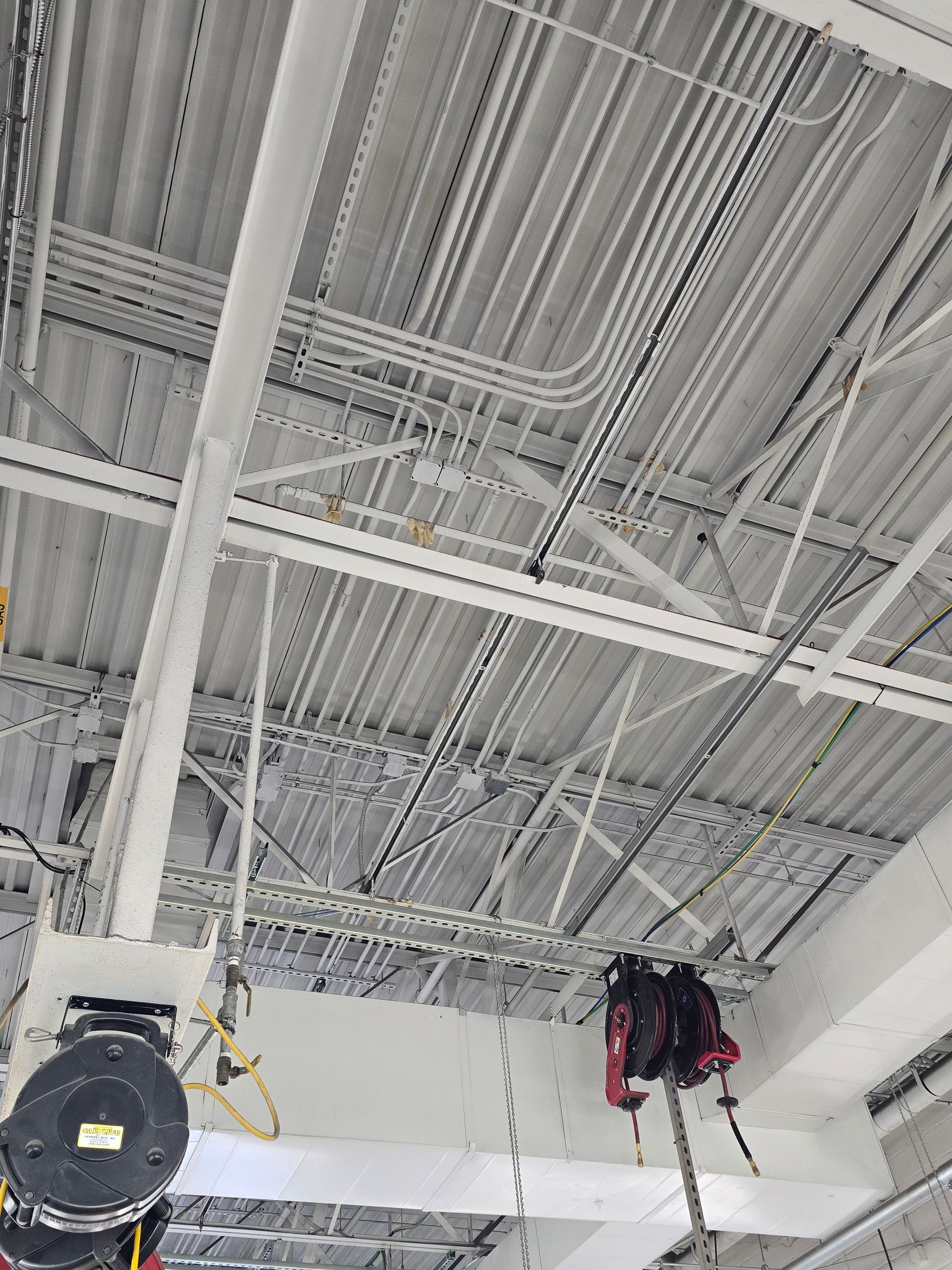 Ceiling of an industrial space with exposed ducts, pipes, and hanging equipment.