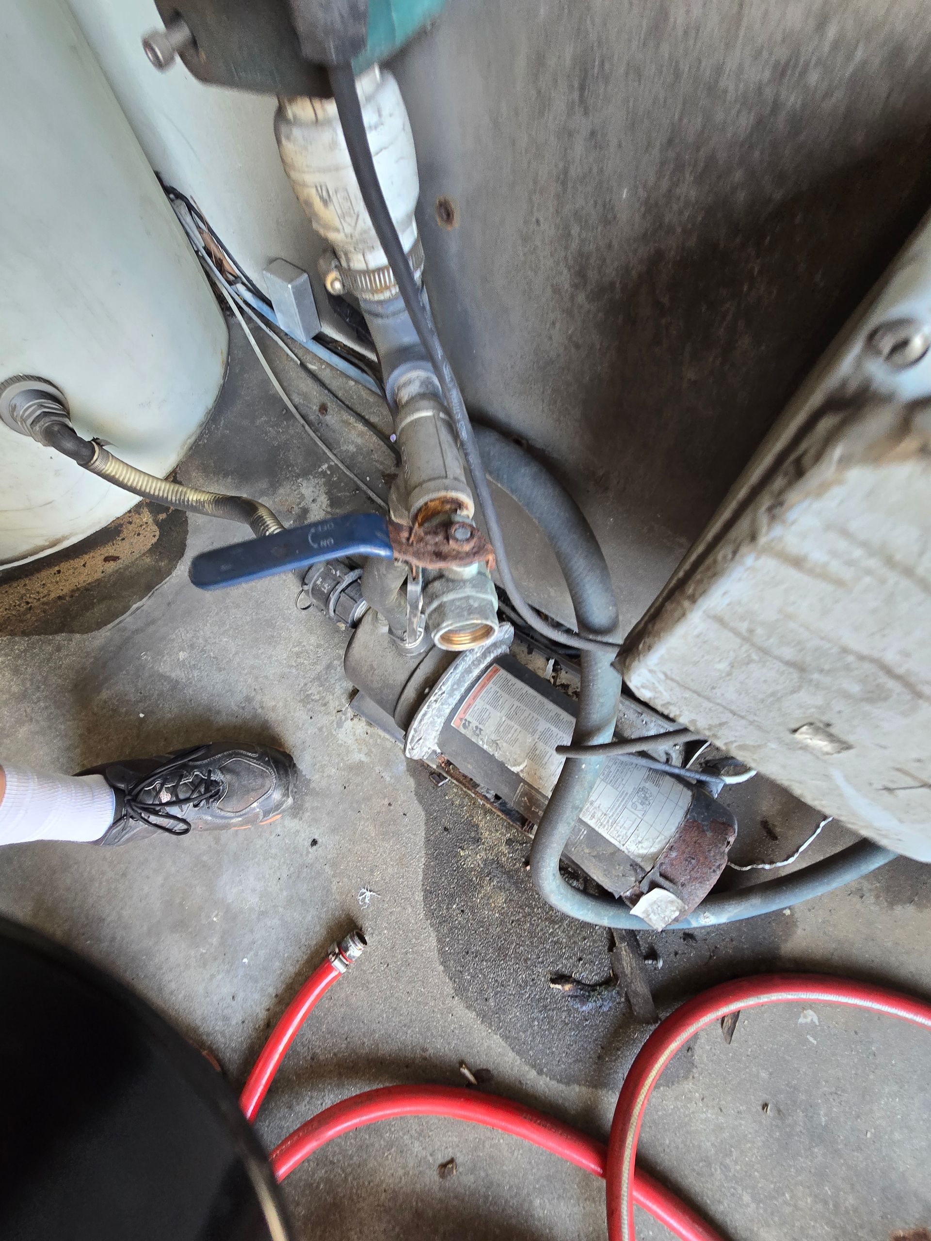 Close-up of corroded plumbing valves and pipes beside a wall, with red hose on a concrete floor