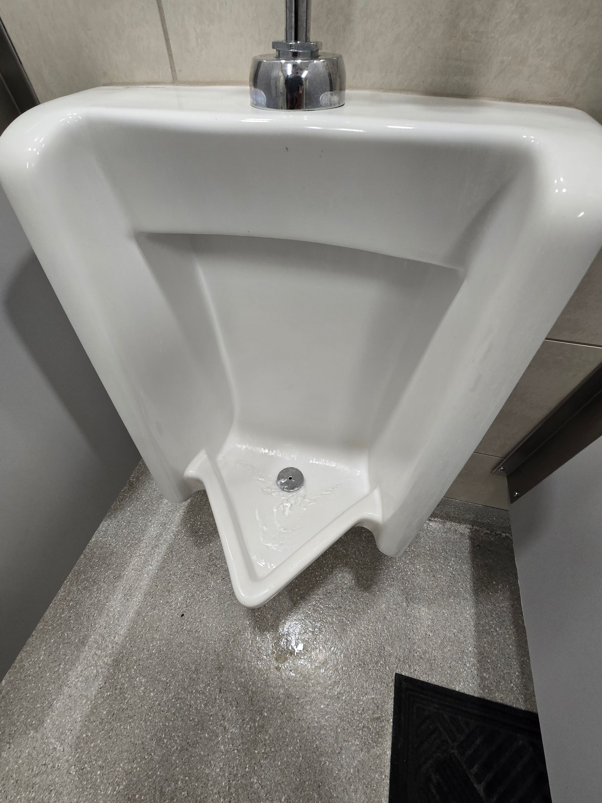 White wall-mounted urinal in a restroom with a gray floor and chrome flush valve