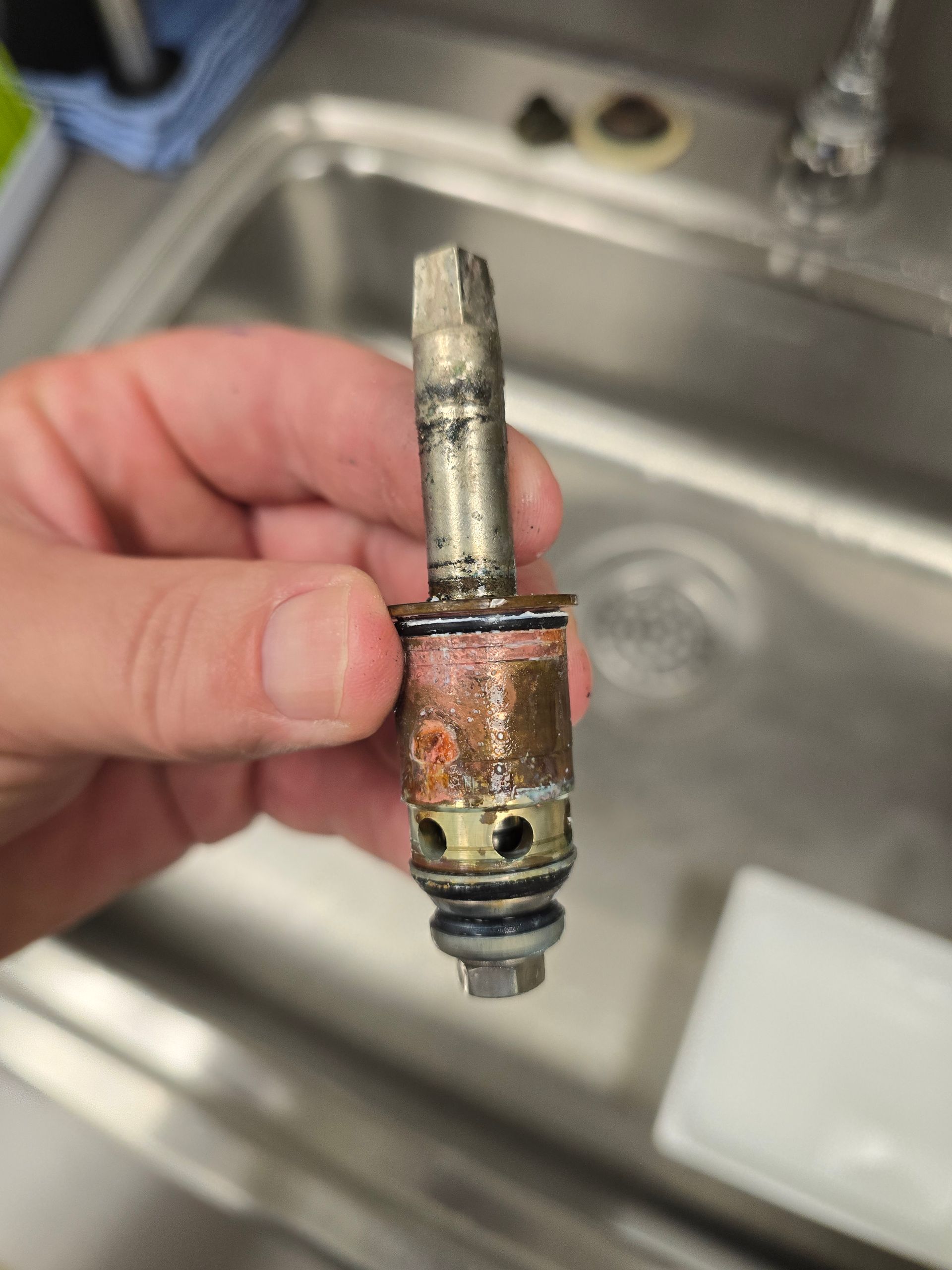 Hand holding a corroded metal plumbing valve part over a sink