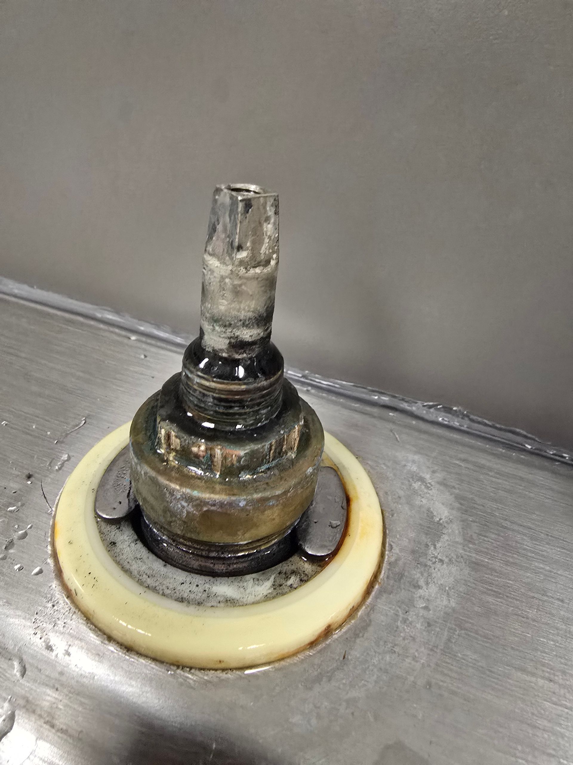 Close-up of a corroded metal valve stem with a white plastic ring on a gray surface.