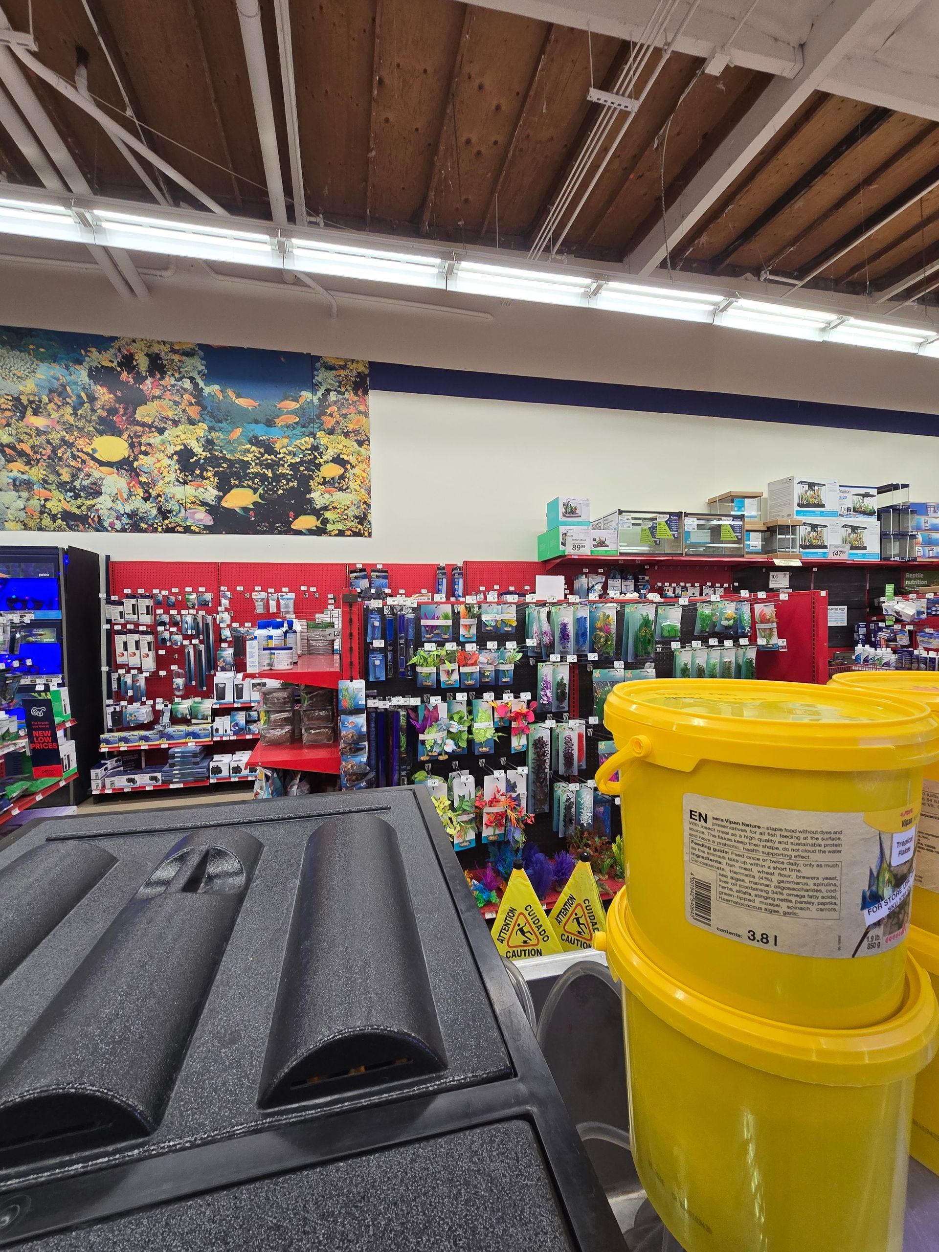 Hardware store aisle with yellow buckets, black pipes, and shelves of tools and supplies